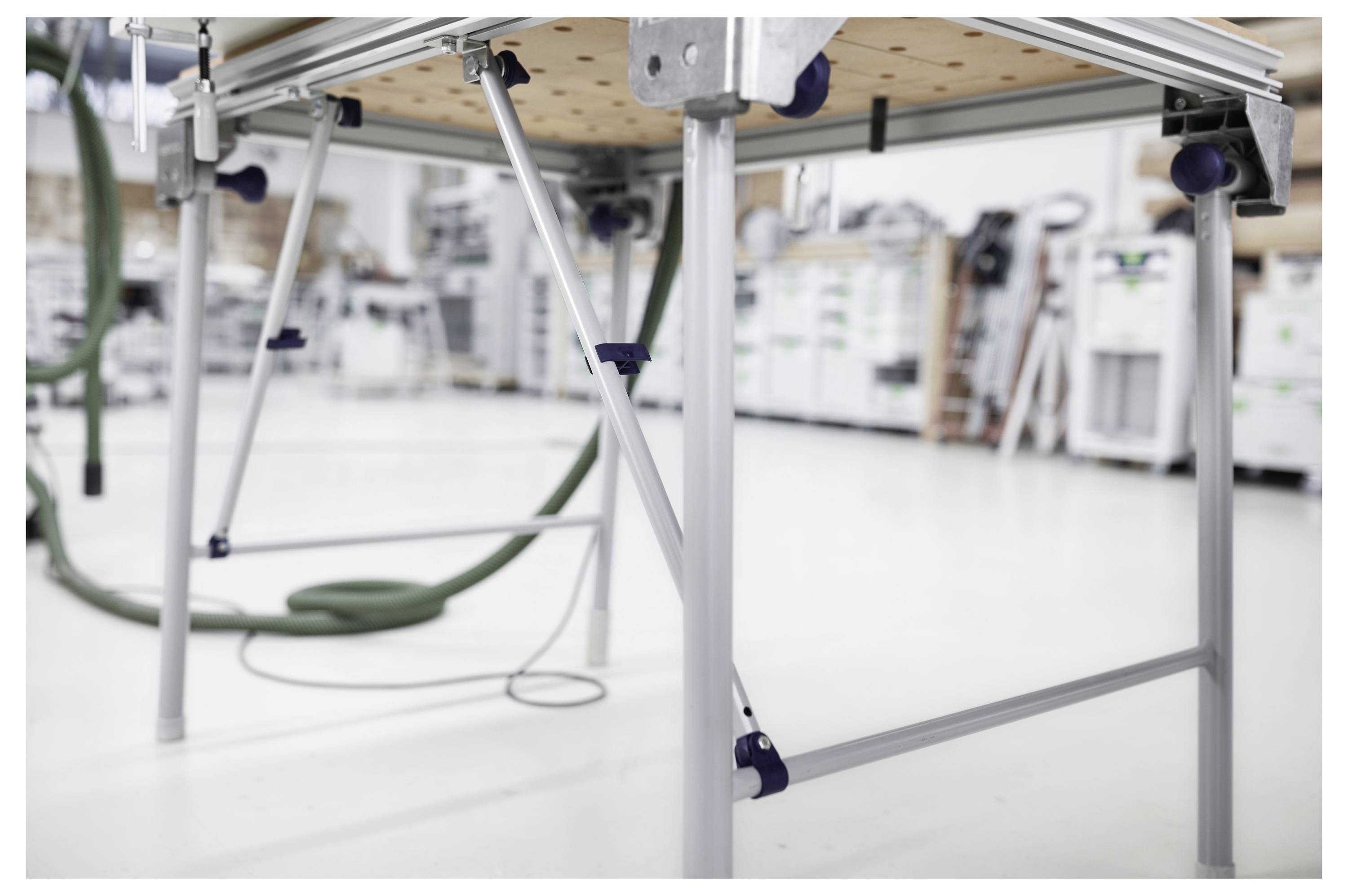 Dłoń trzymająca elektronarzędzie marki Festool wyposażone w wąż, demonstrująca jego użycie do cięcia przez deskę drewna, pokazująca precyzję.