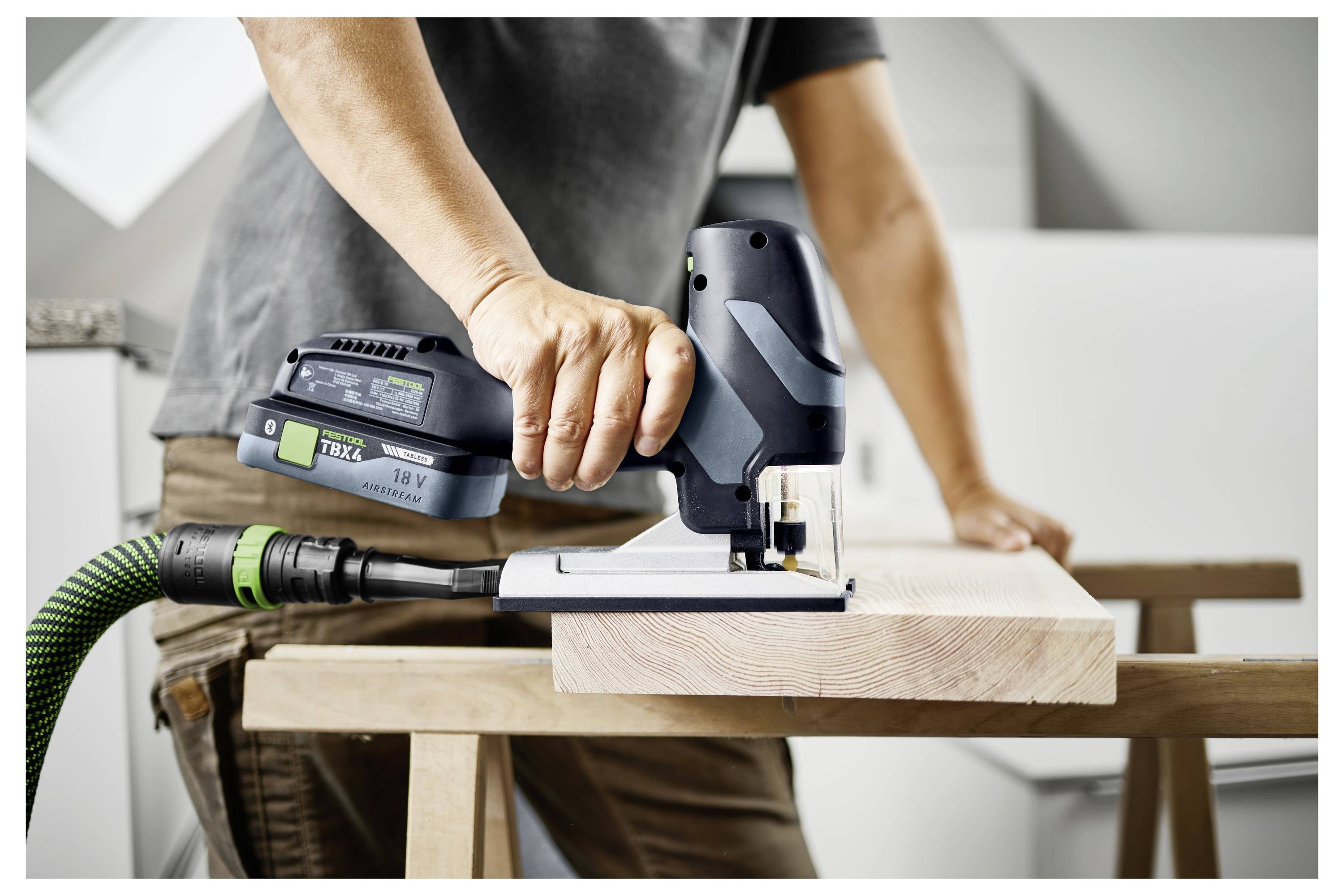 Osoba używa bezprzewodowej piłki do wycinania drewna na warsztacie, demonstrując pracę związaną z ulepszaniem domu lub cieśliną.