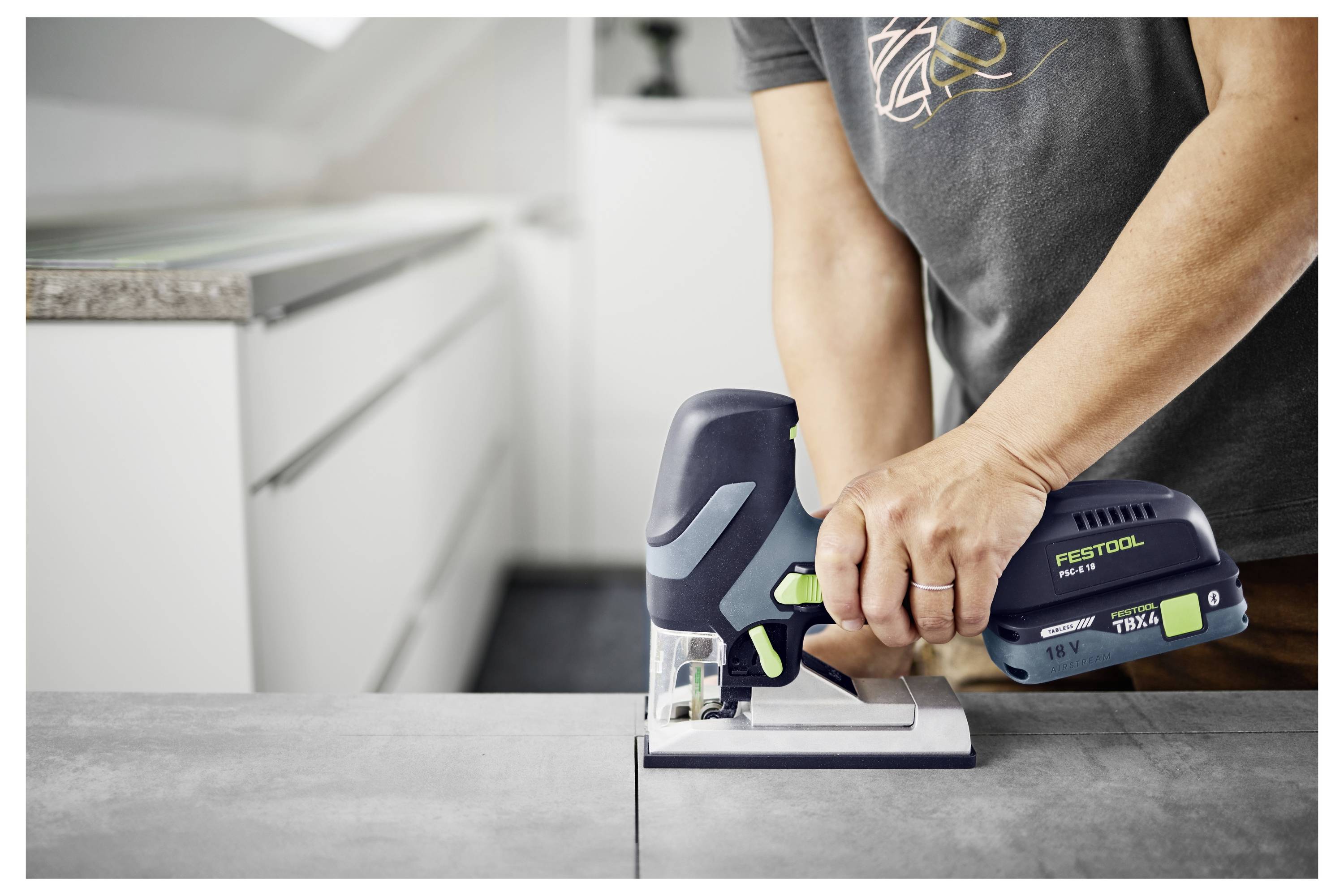 Osoba używa piły elektrycznej Festool do cięcia kawałka drewna na stole w nowoczesnej kuchni.