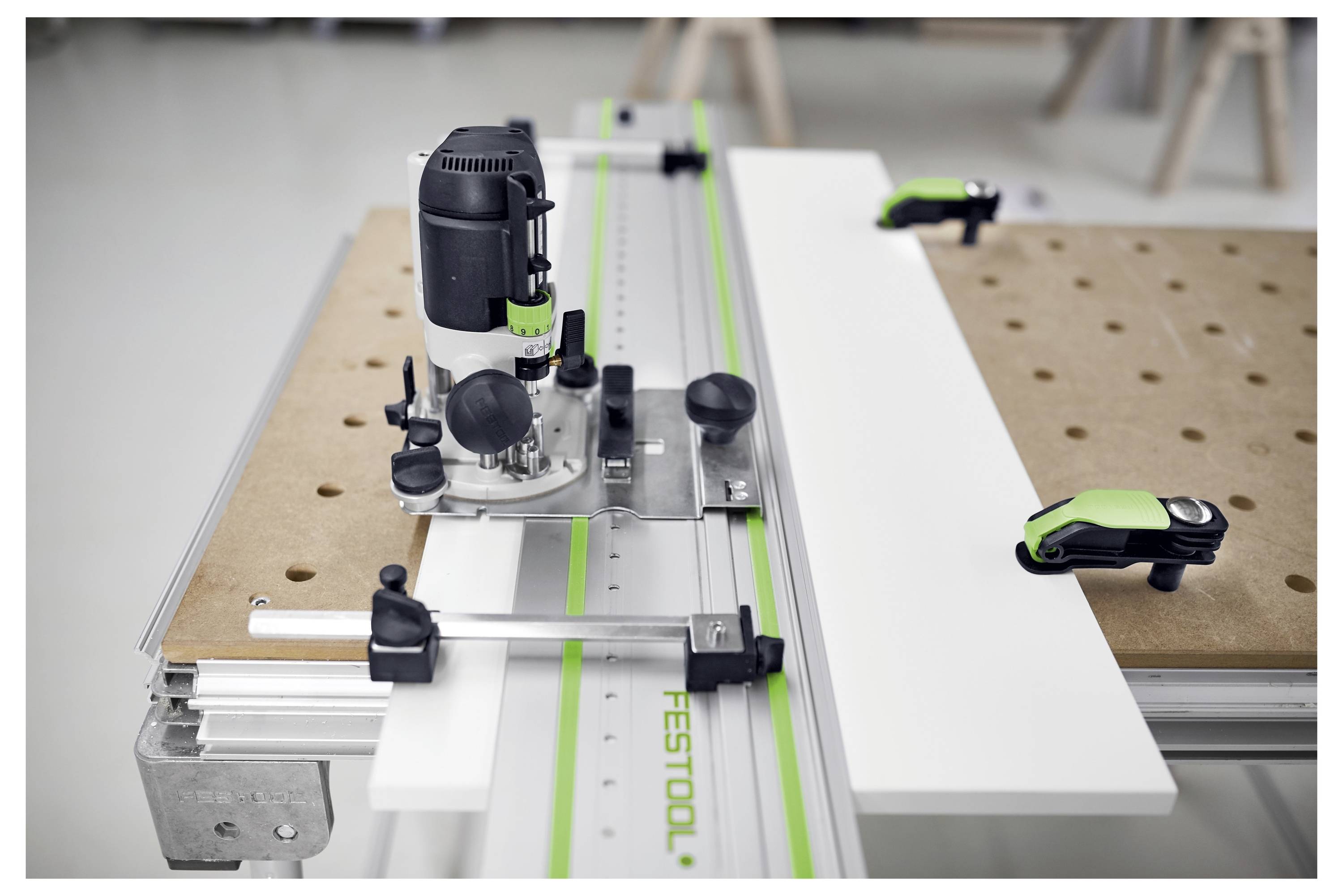 System routera i szyny przewodniej na stole roboczym z zaciskami, sugerujący precyzyjne obróbkę lub pracę drewniarską w otoczeniu warsztatu.