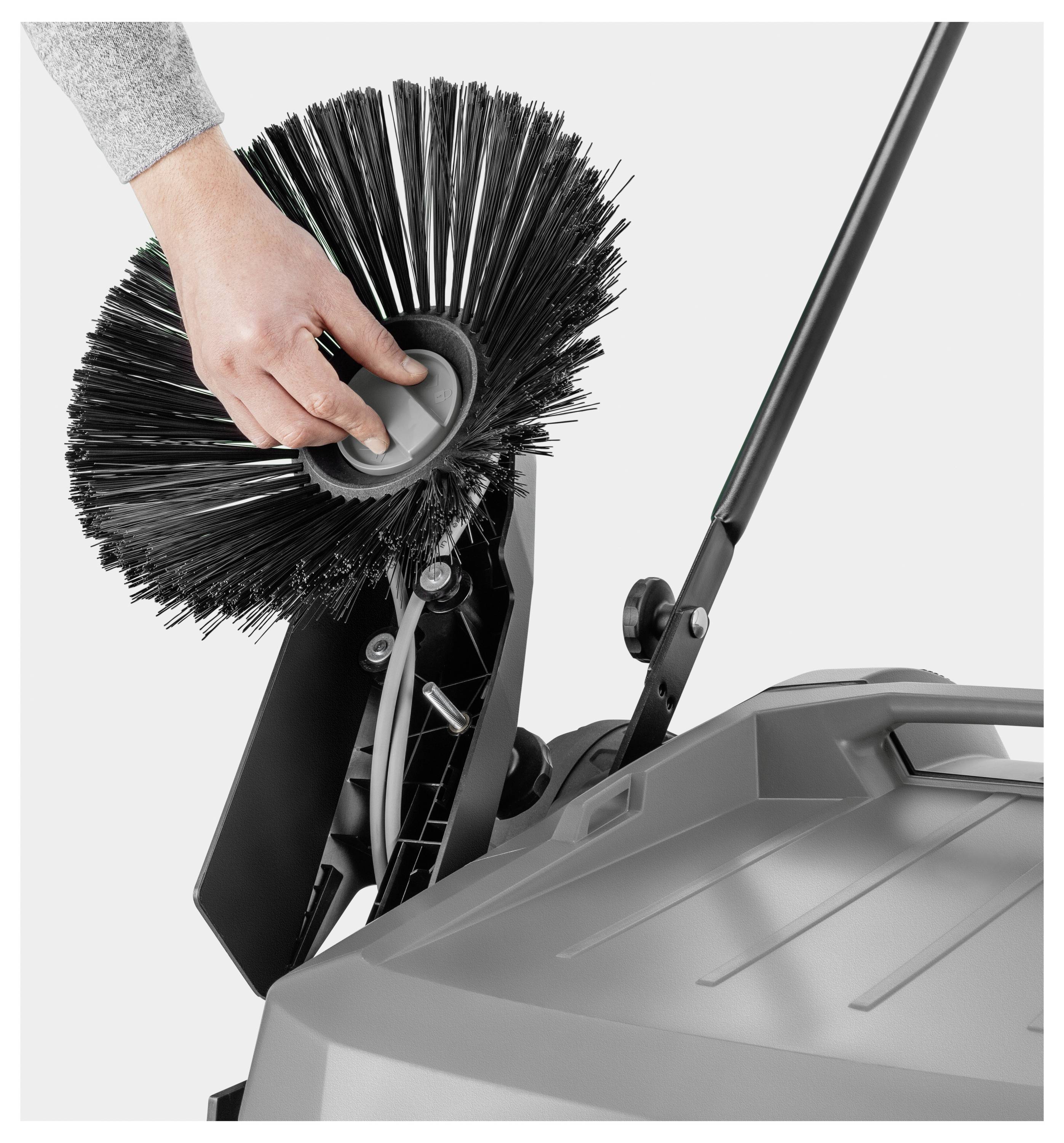 Ręka regulująca szczotkę szarej maszyny czyszczącej z czarnym uchwytem, pokazująca zbliżony widok mechanizmu szczotki.