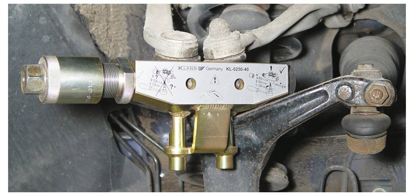 Zbliżenie obrazu mechanicznego narzędzia przymocowanego do części zawieszenia samochodu. Narzędzie ma grawerowania wskazujące, że jest produkcji niemieckiej.
