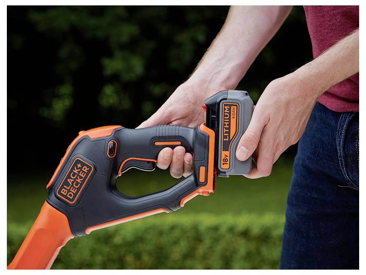 'Osoba wkłada baterię litową 18V do narzędzia ogrodowego BLACK+DECKER na tle rozmytego naturalnego krajobrazu.'