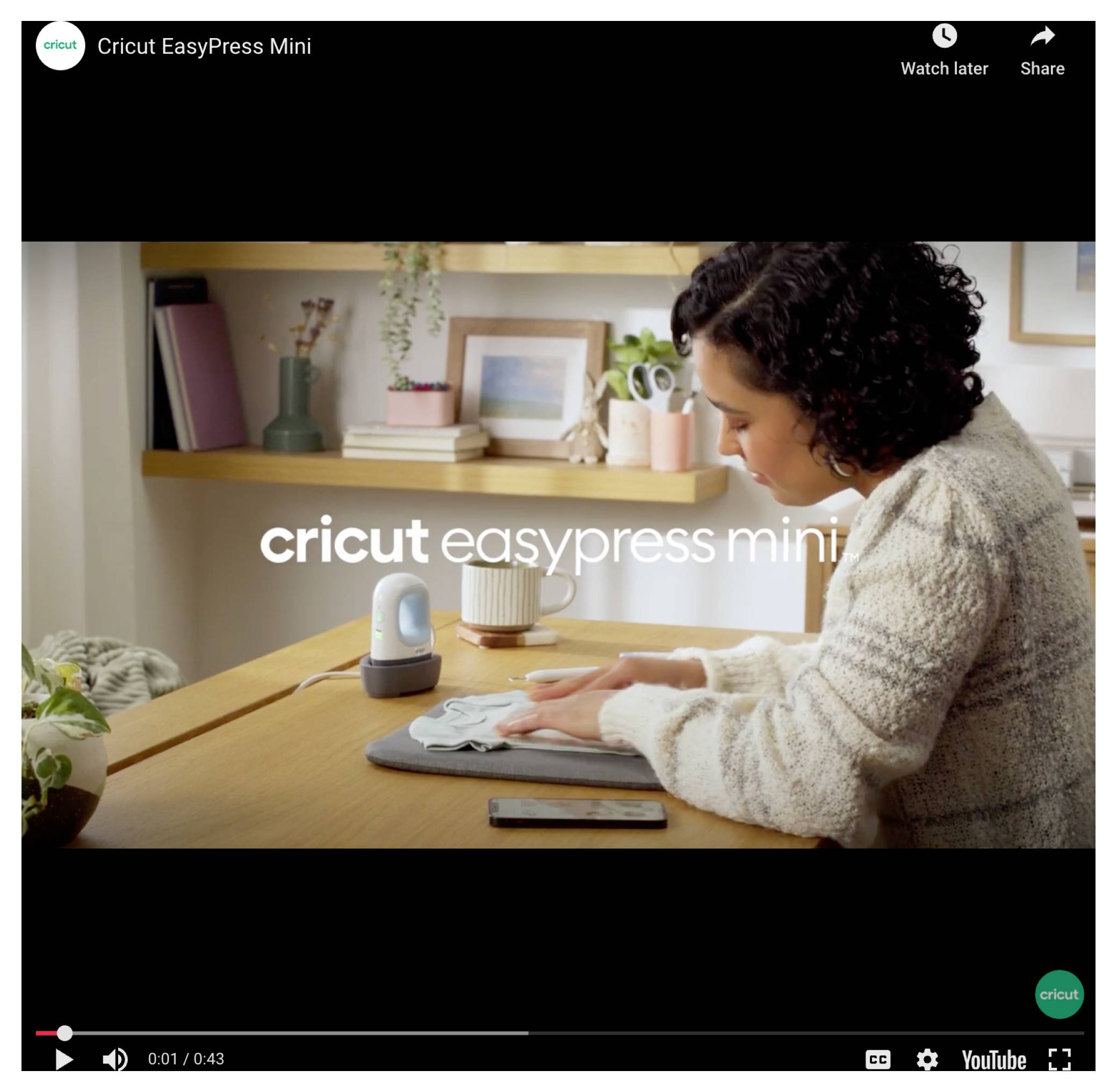 Kobieta siedzi przy stole i używa małej prasy do aplikacji, aby nanieść wzór na tkankę. Na ekranie widnieje napis „Cricut EasyPress Mini".