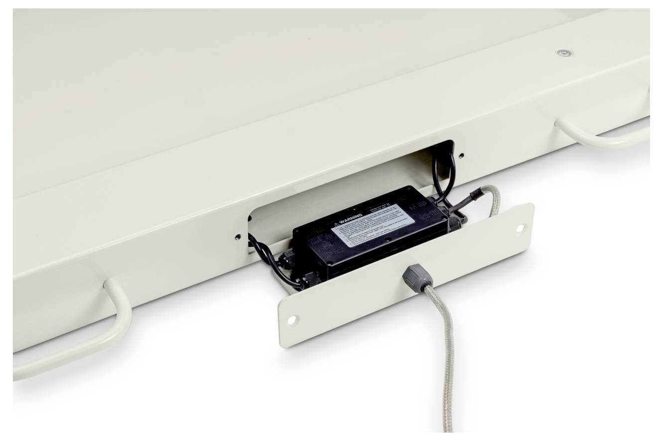 'Zbliżony widok jednostki zasilania podłączonej do przewodów, umieszczonej w otwartym przedziale na białej powierzchni, z uchwytami po obu stronach.'