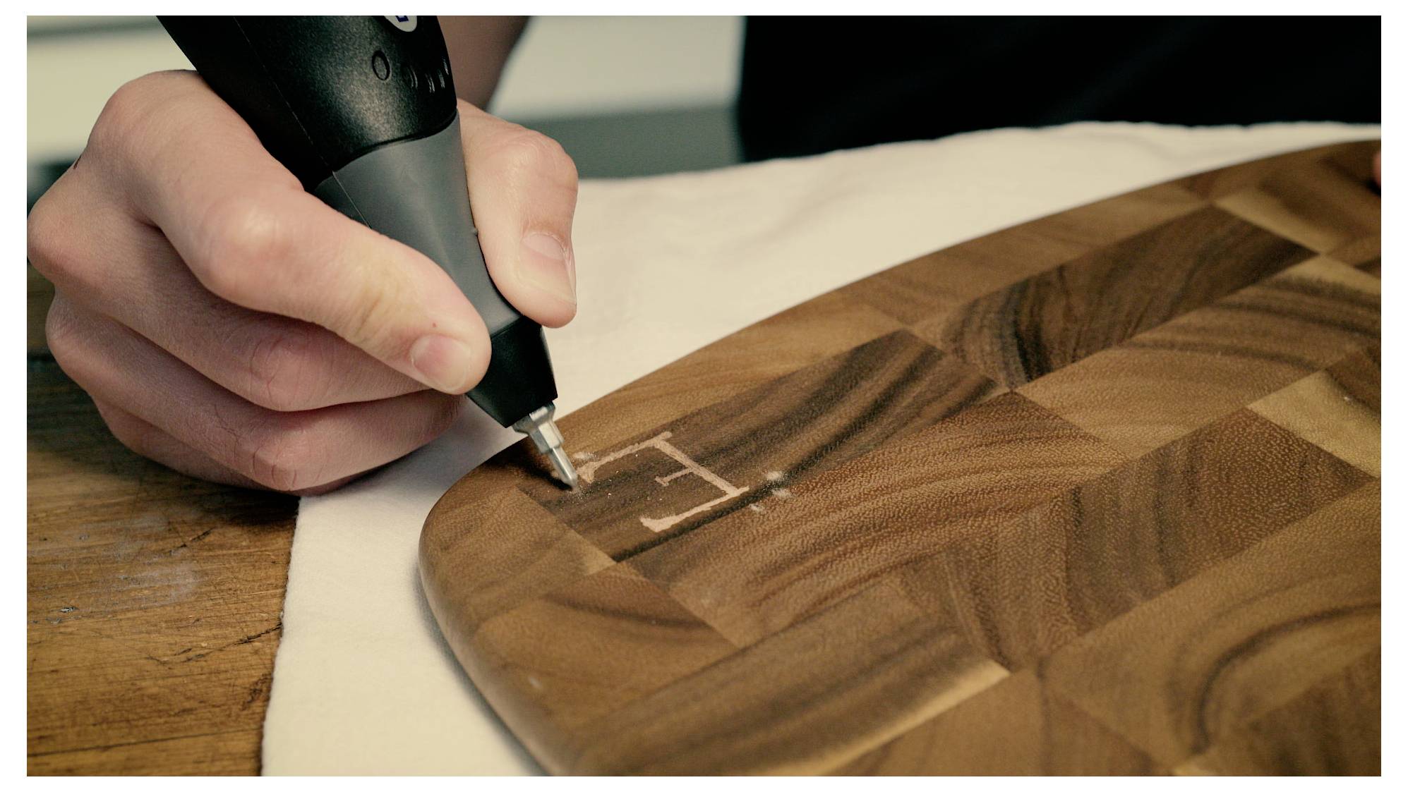 Ręka z narzędziem wygrawerowaną literę "E" na drewnianej powierzchni, demonstrując rzemiosło lub projekt obróbki drewna w trakcie realizacji.