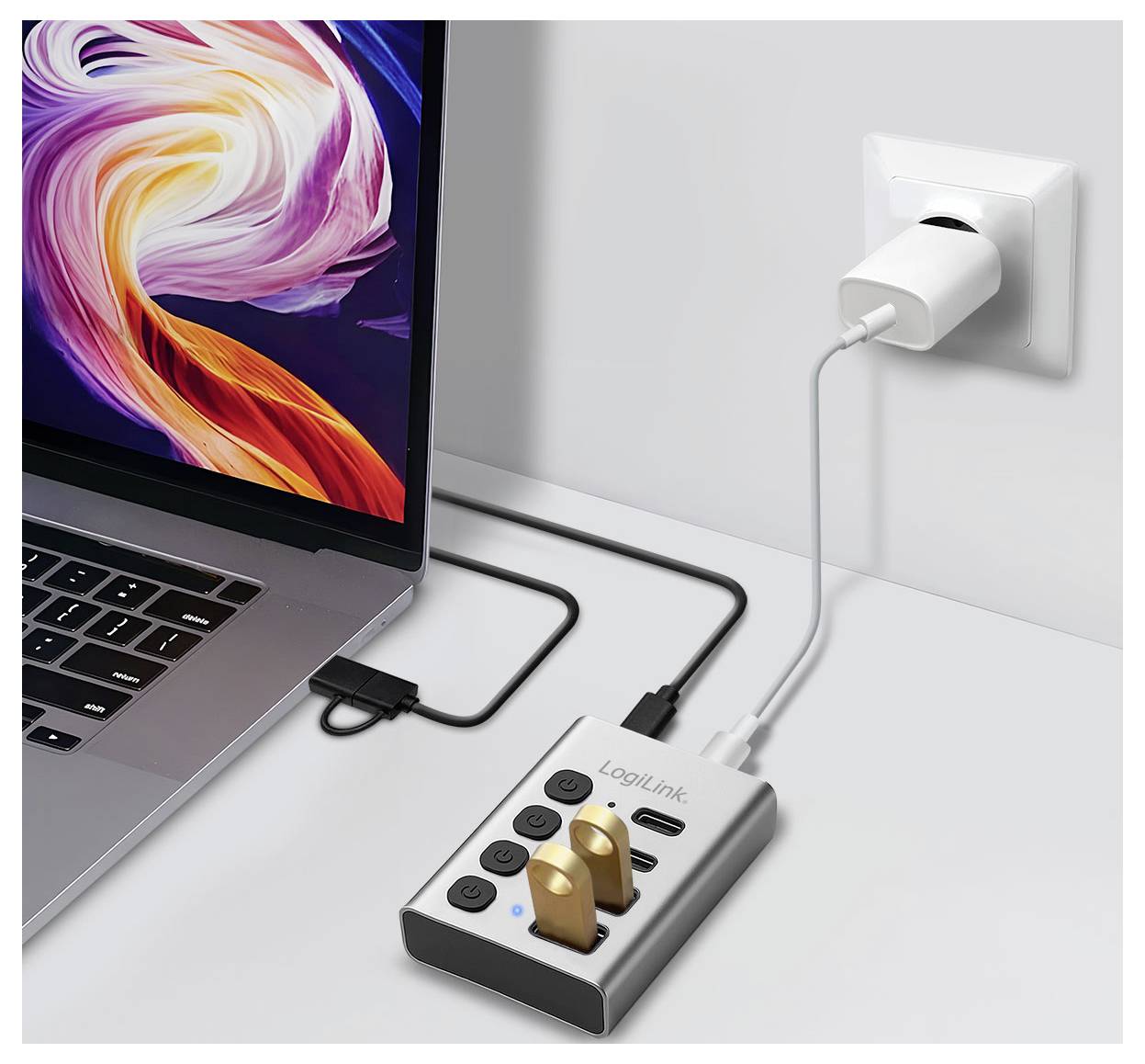 Laptop podłączony do gniazda ściennego poprzez hub USB-C/listwa zasilająca z dwoma włączonymi przewodami i dołączonym kablem ładującym.