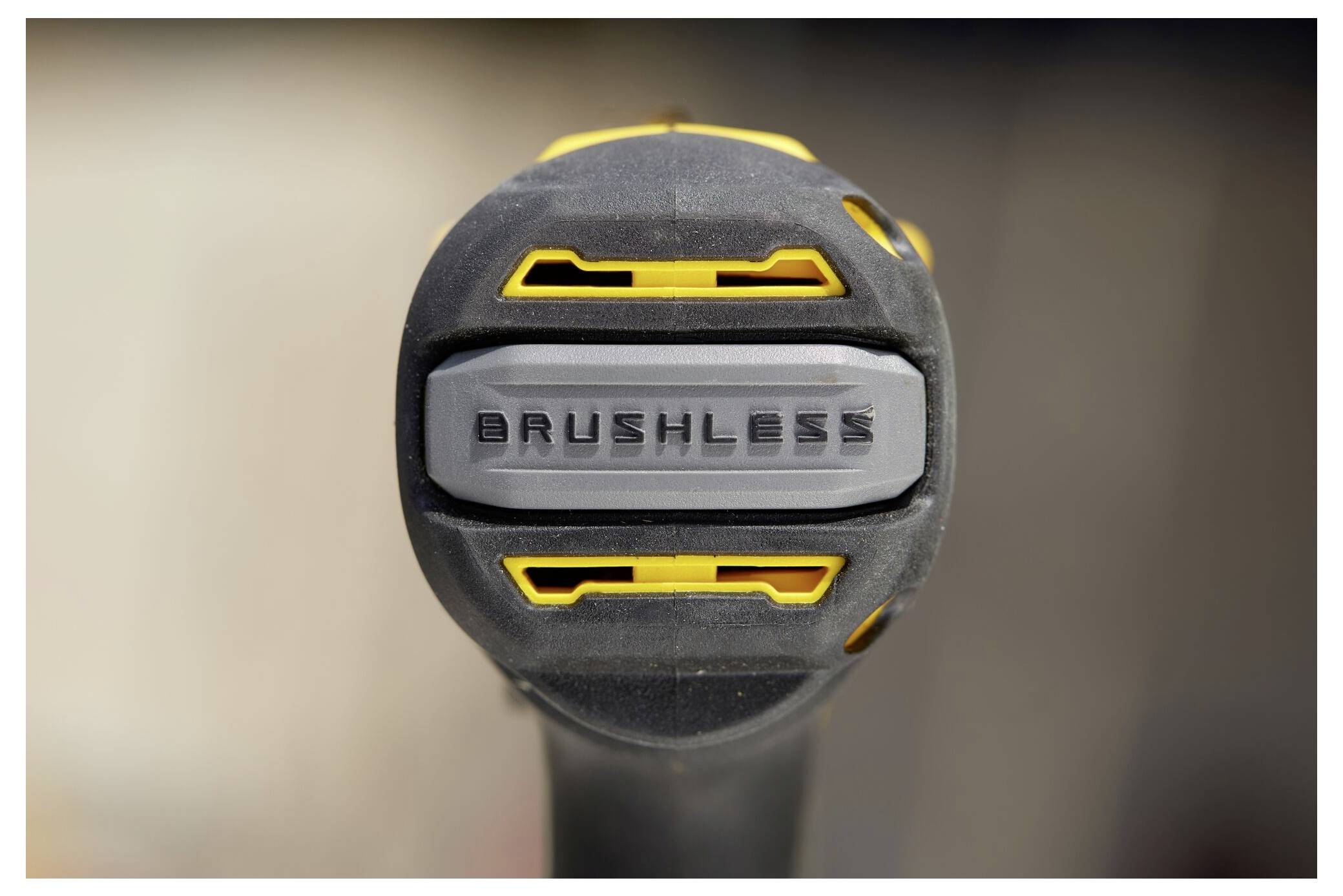 Zbliżenie uchwytu narzędzia z etykietą "BRUSHLESS" w środku, z żółtymi akcentami na szarym i czarnym tle.