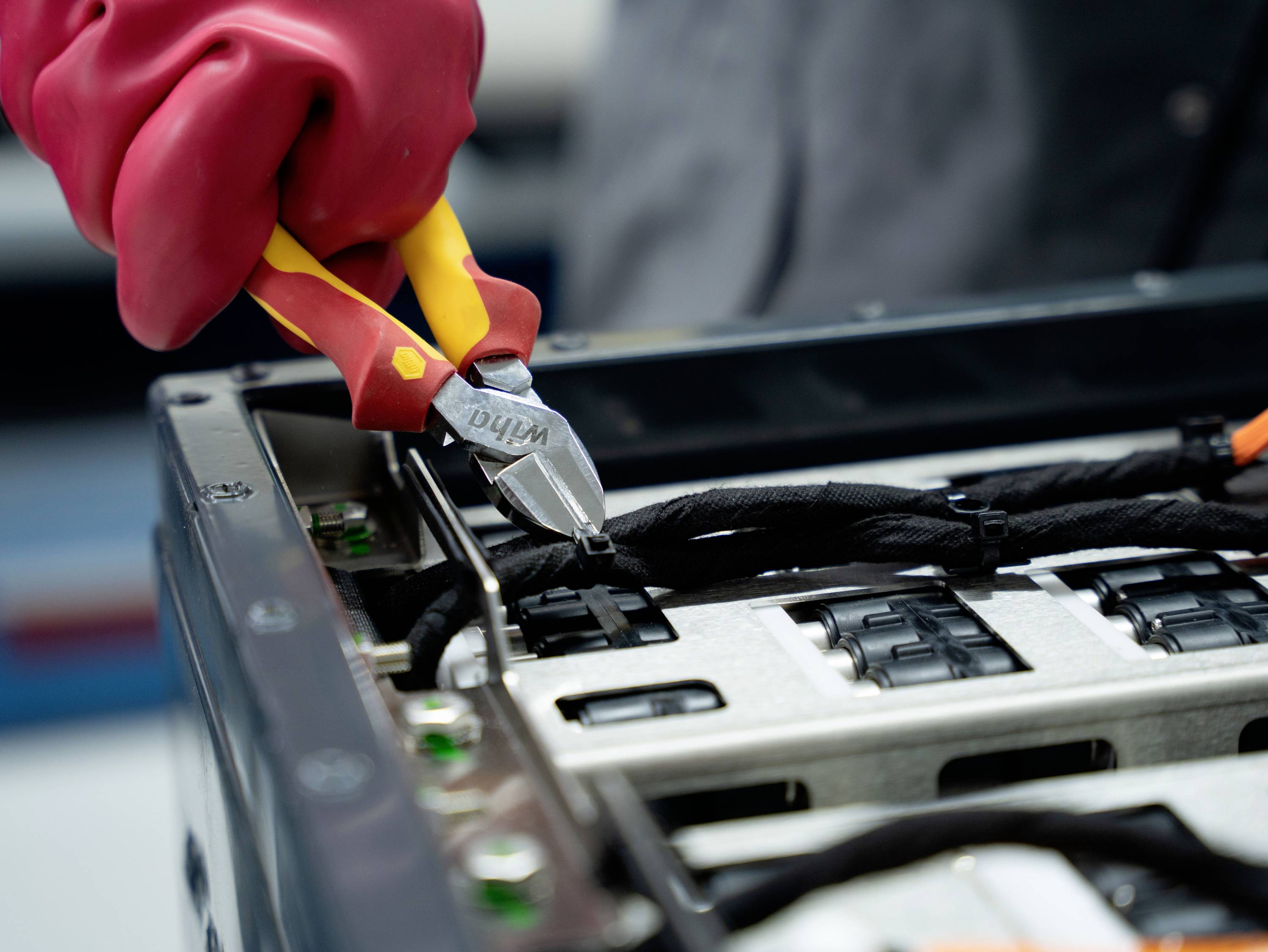 Rękawiczkowana dłoń przy użyciu obcinacza drutu przecina kable wewnątrz otwartej urządzenia elektronicznego lub obudowy serwera.