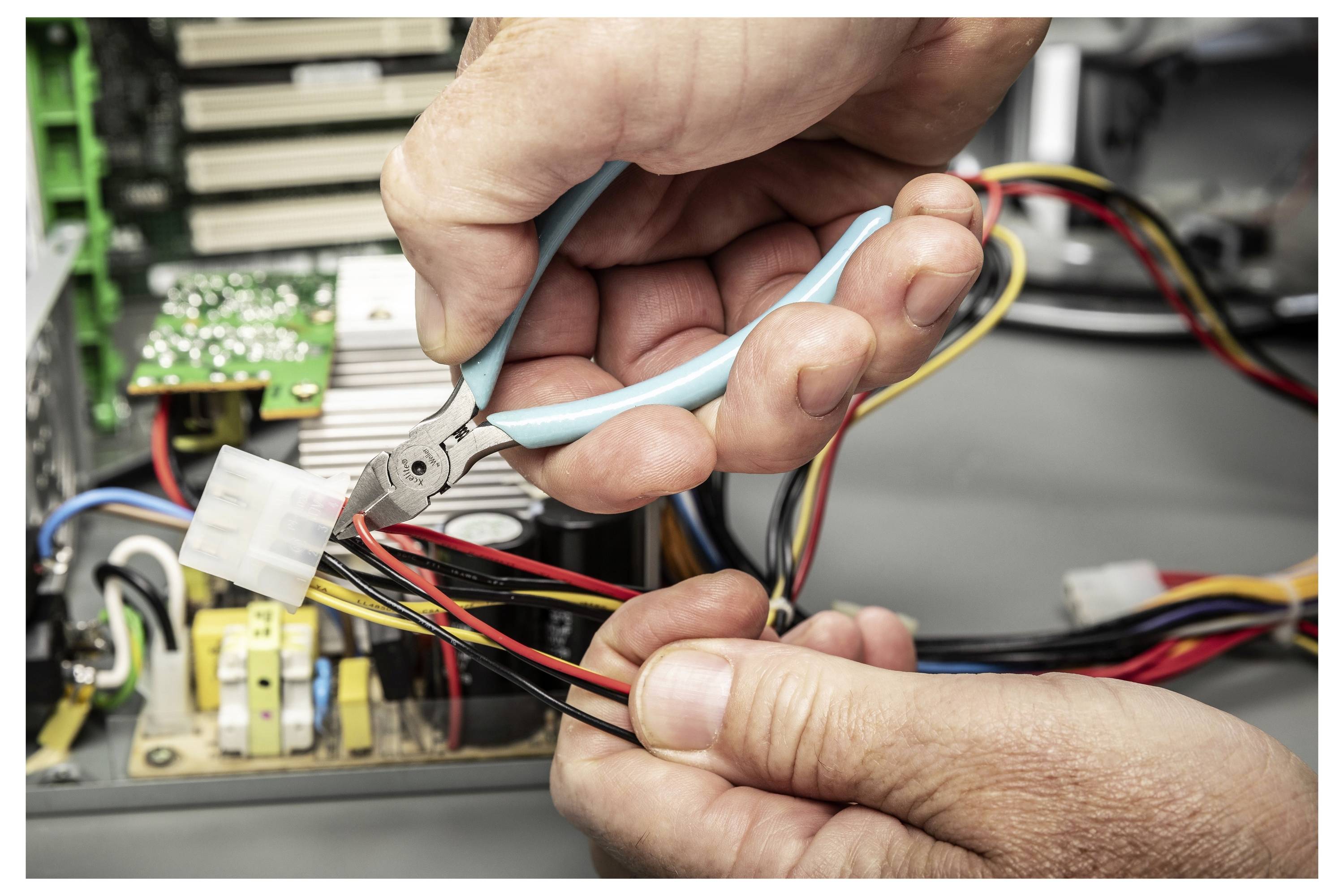 Ręce używające szczypiec do cięcia lub zdejmowania izolacji z przewodów wewnątrz otwartego urządzenia elektronicznego podczas naprawy.
