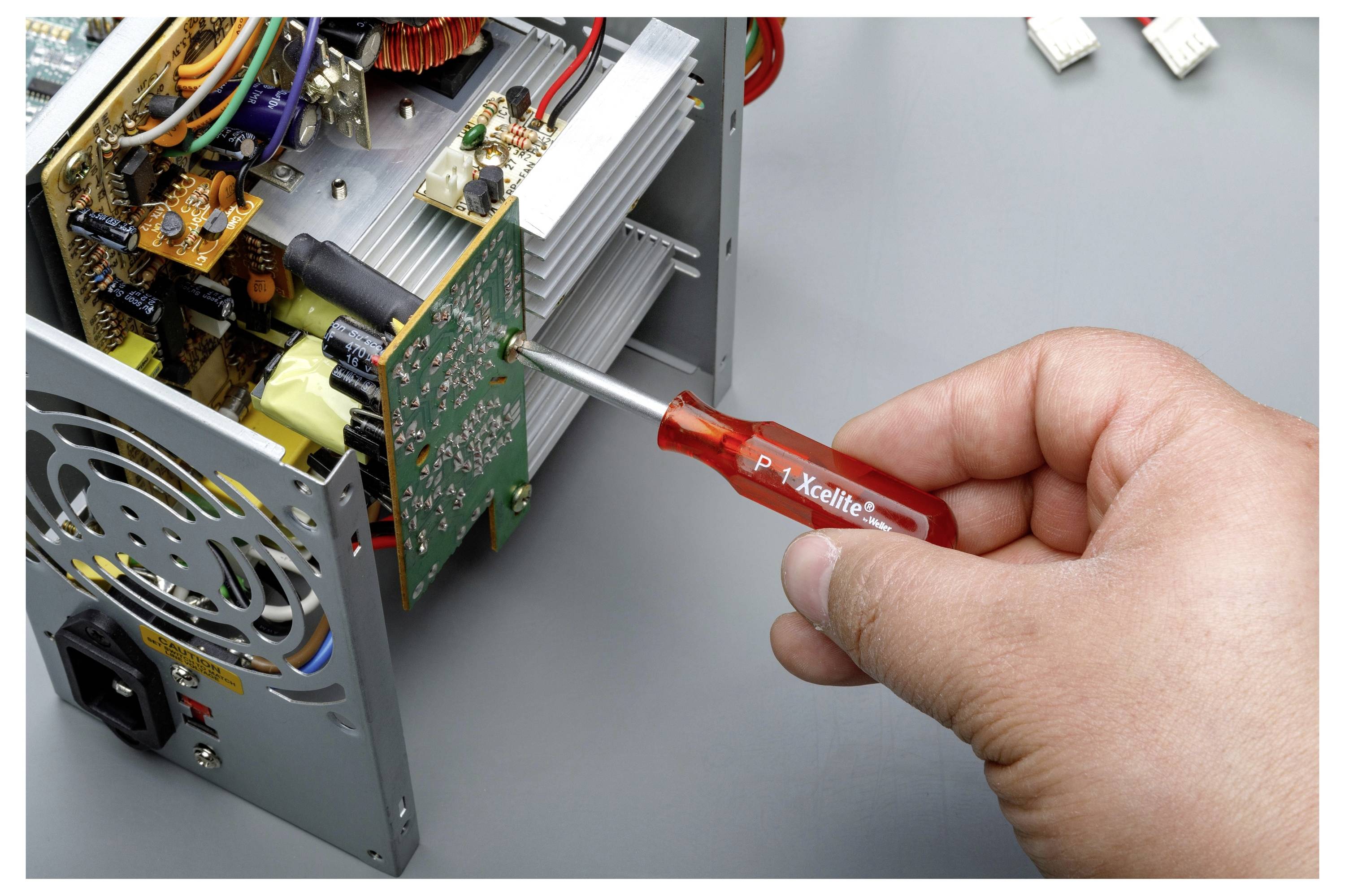 Ręka używająca śrubokrętu do regulacji otwartego urządzenia elektronicznego z widocznymi płytkami drukowanymi i okablowaniem.