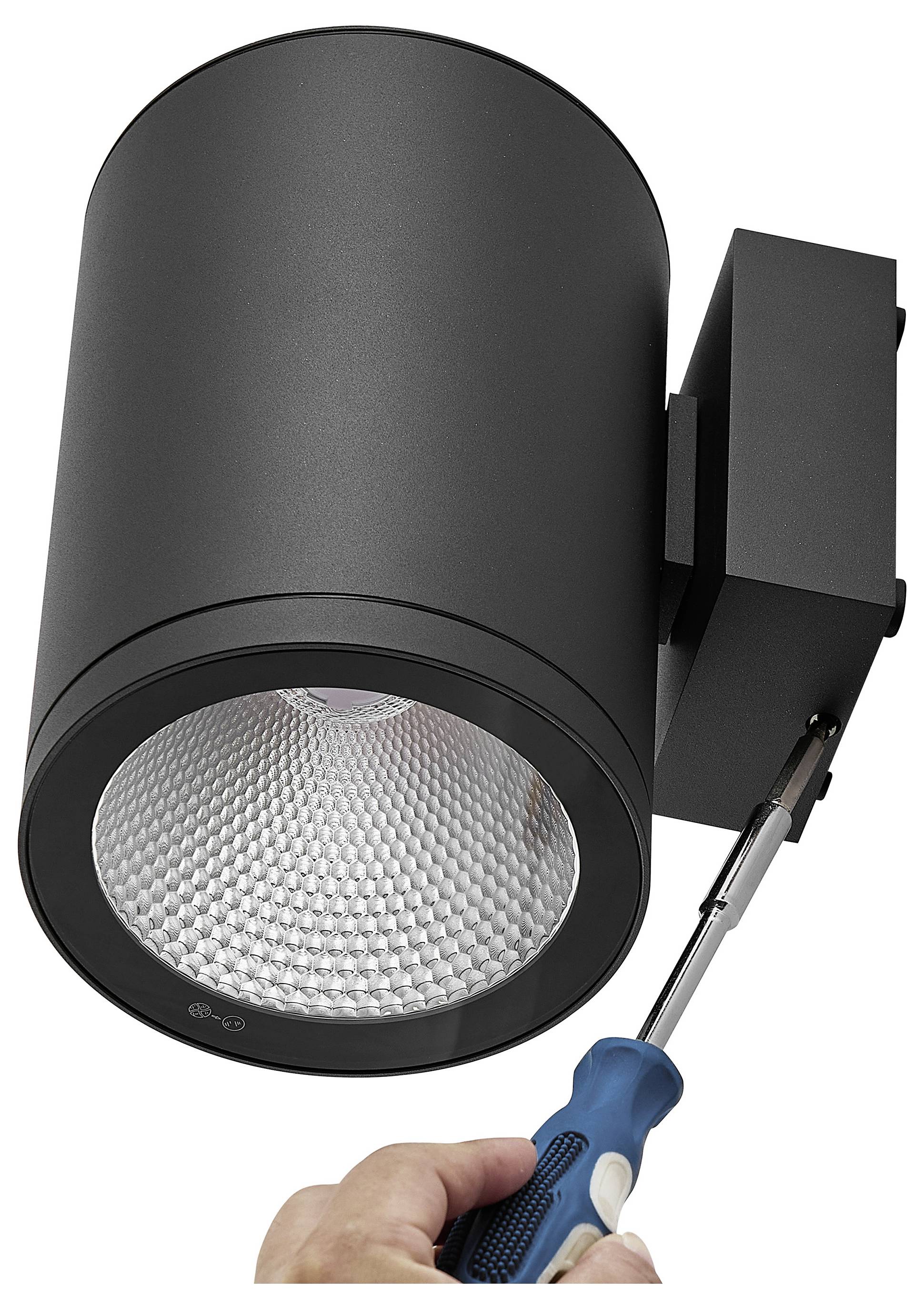Czarna cylindryczna lampa sufitowa będąca instalowana śrubokrętem, pokazująca oprAwę i uchwyt montażowy.