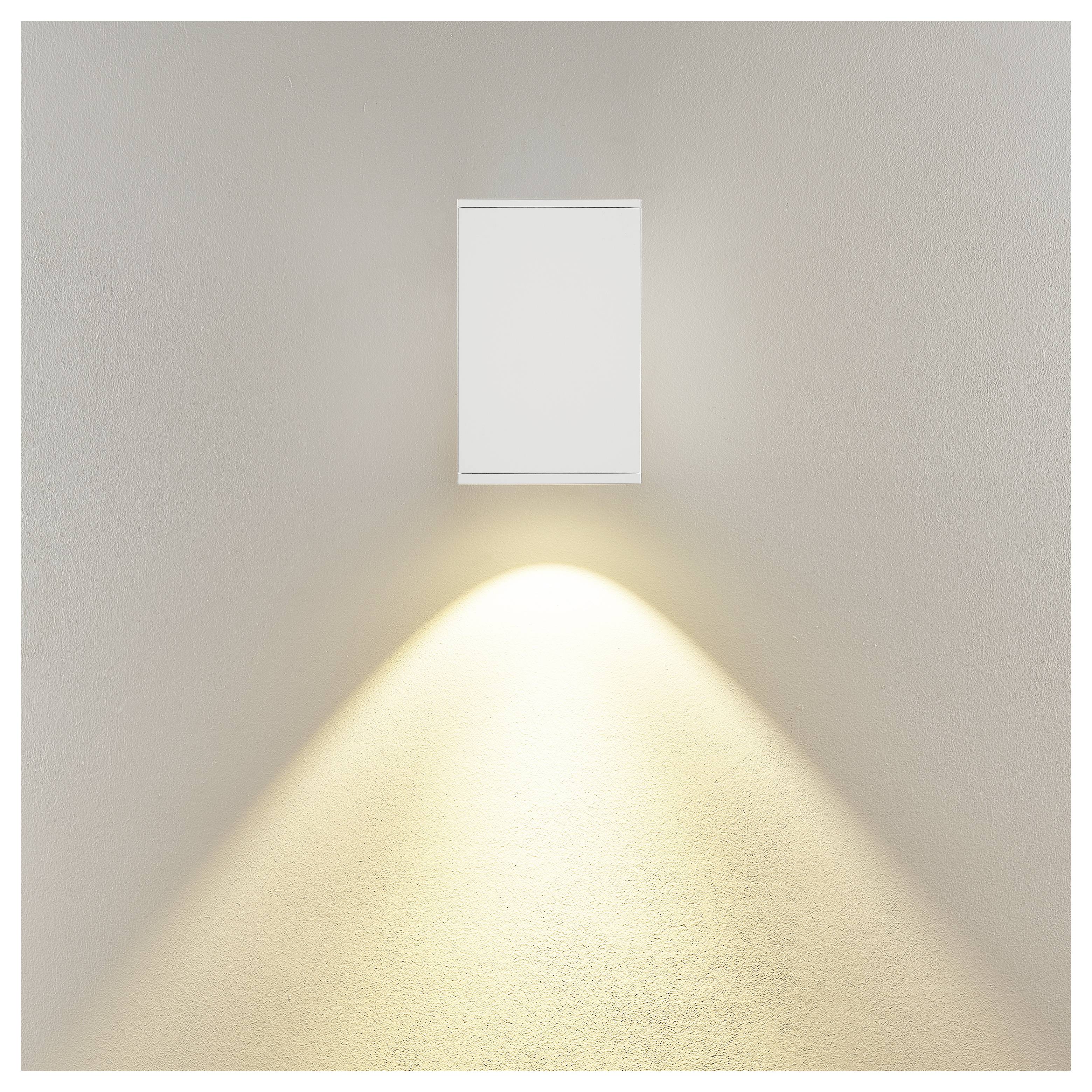 Minimalistyczna lampa ścienna z prostokątnym białym oprawą rzucającą ciepłą trójkątną wiązkę światła w dół na beżową ścianę.