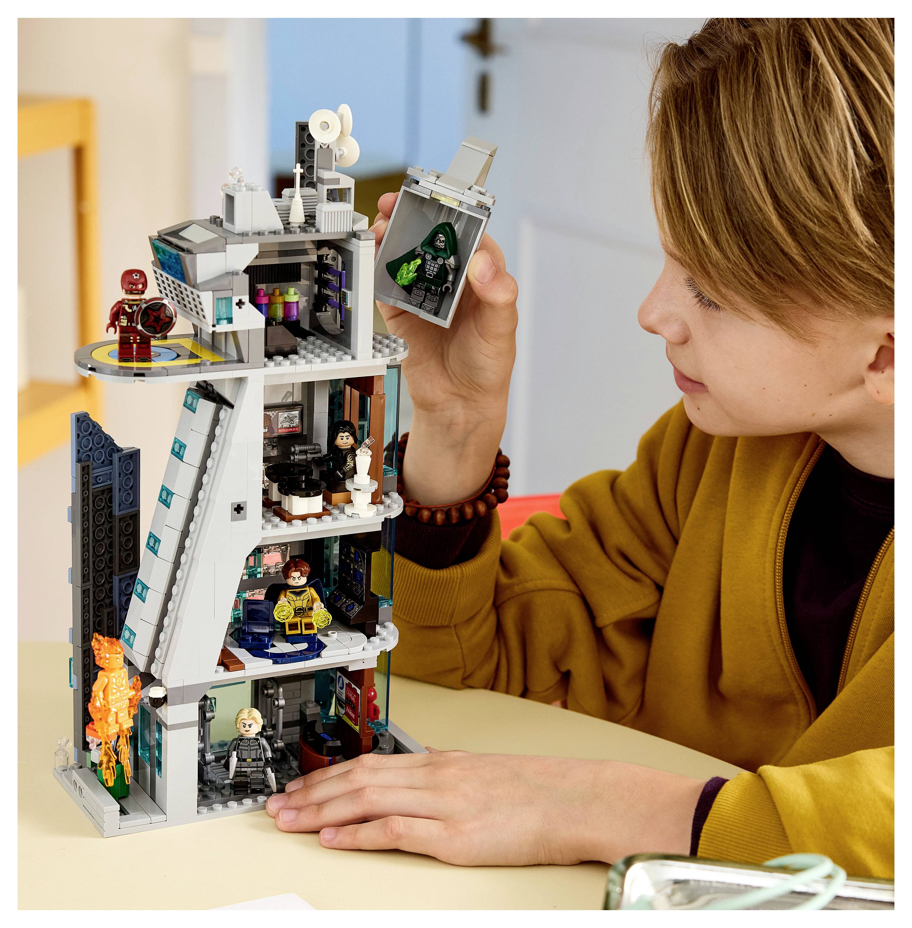 Dziecko bawiące się zestawem wysokościowca w stylu LEGO, trzymające część minifigurki i patrzące na zbudowany model na stole.