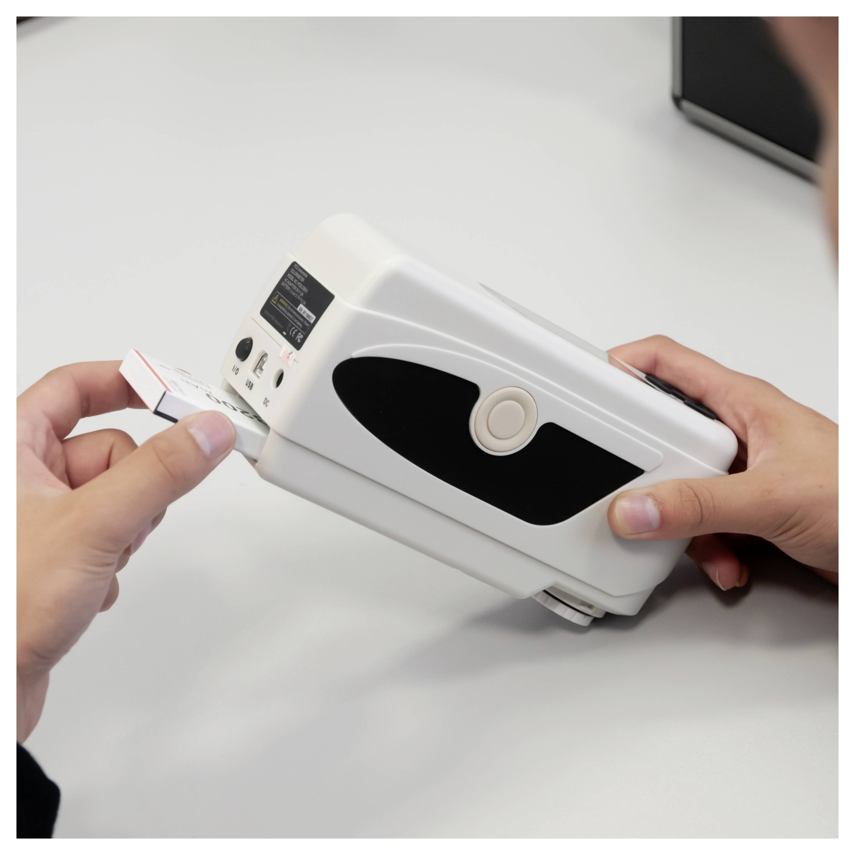 Ręce zasilają drukarkę białej etykiety, gdy drukuje ona małą etykietę na białym biurku.