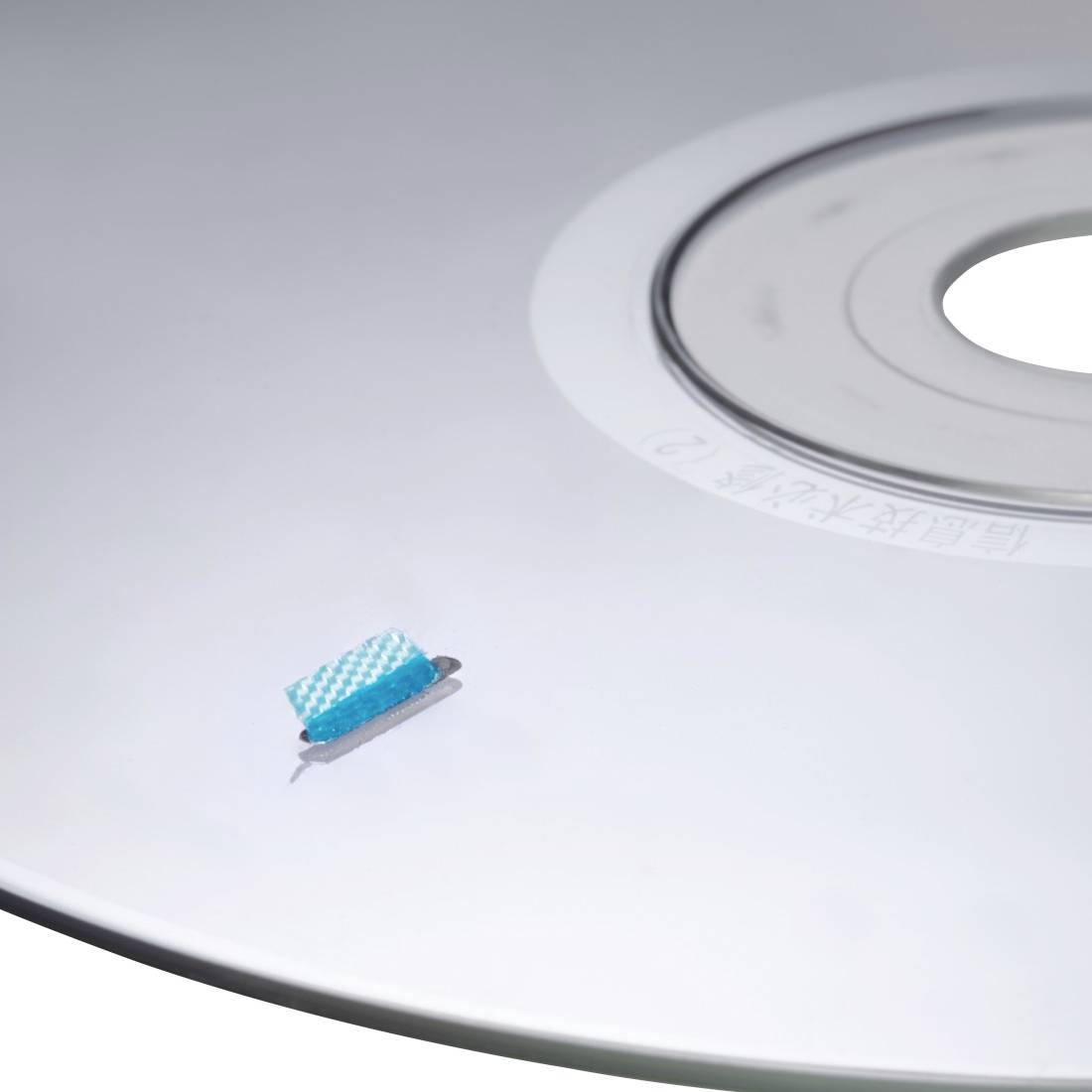 Niebieska szczotka do czyszczenia spoczywa na białej płycie CD lub DVD blisko centralnego otworu.