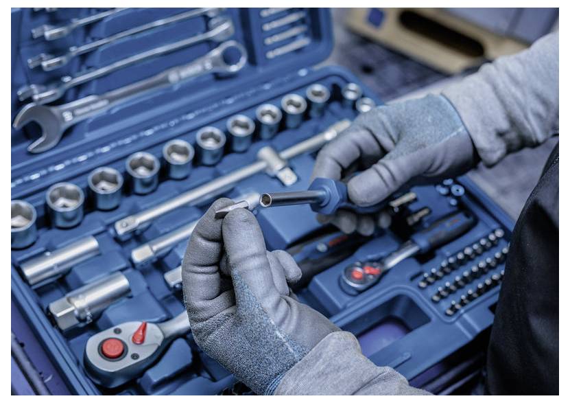 Rękawiczki inspekcjonują metalowe gniazdo w niebieskim mechanicznym zestawie narzędzi z kluczami, gniazdami i kluczami dynamometrycznymi ułożonymi w etui.