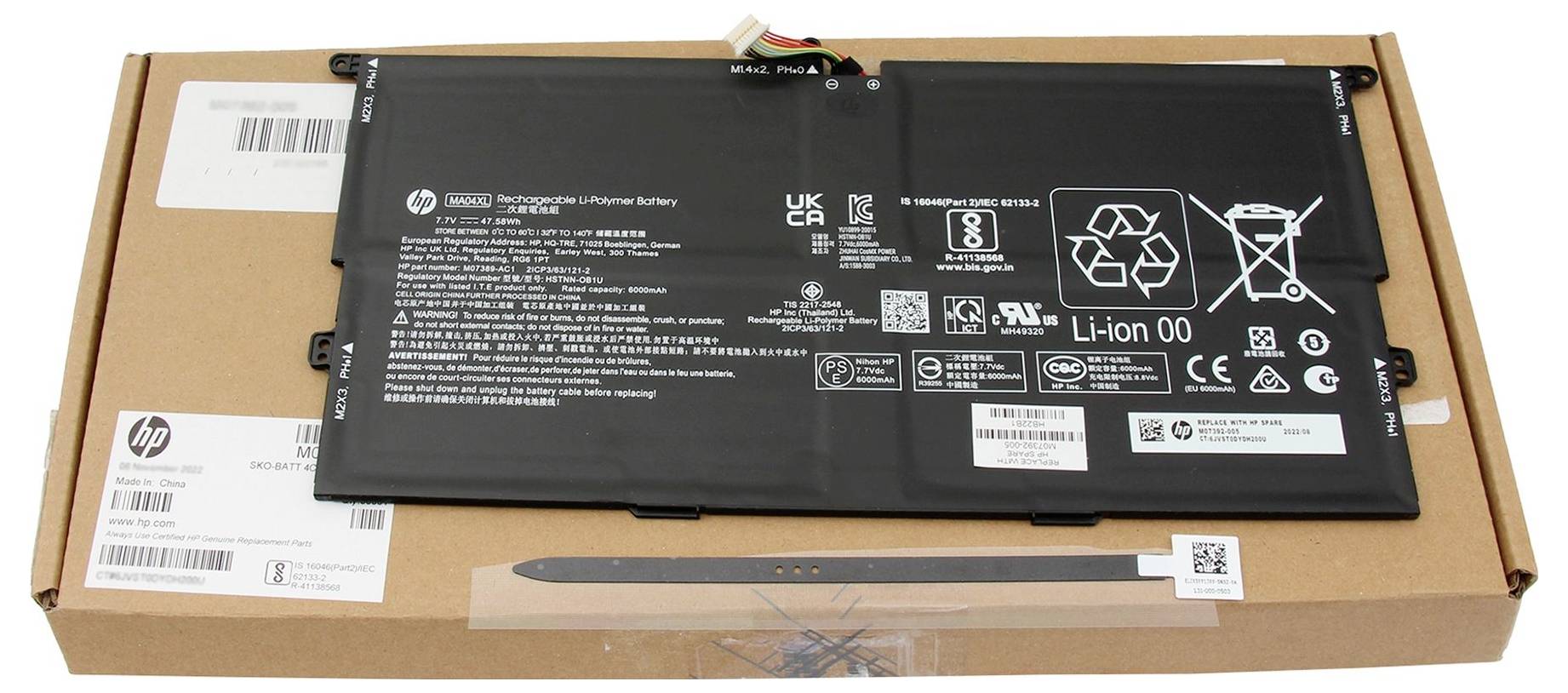Czarna bateria do laptopa położona na pudełku kartonowym do wysyłki HP, z widocznymi etykietami i kodami kreskowymi.