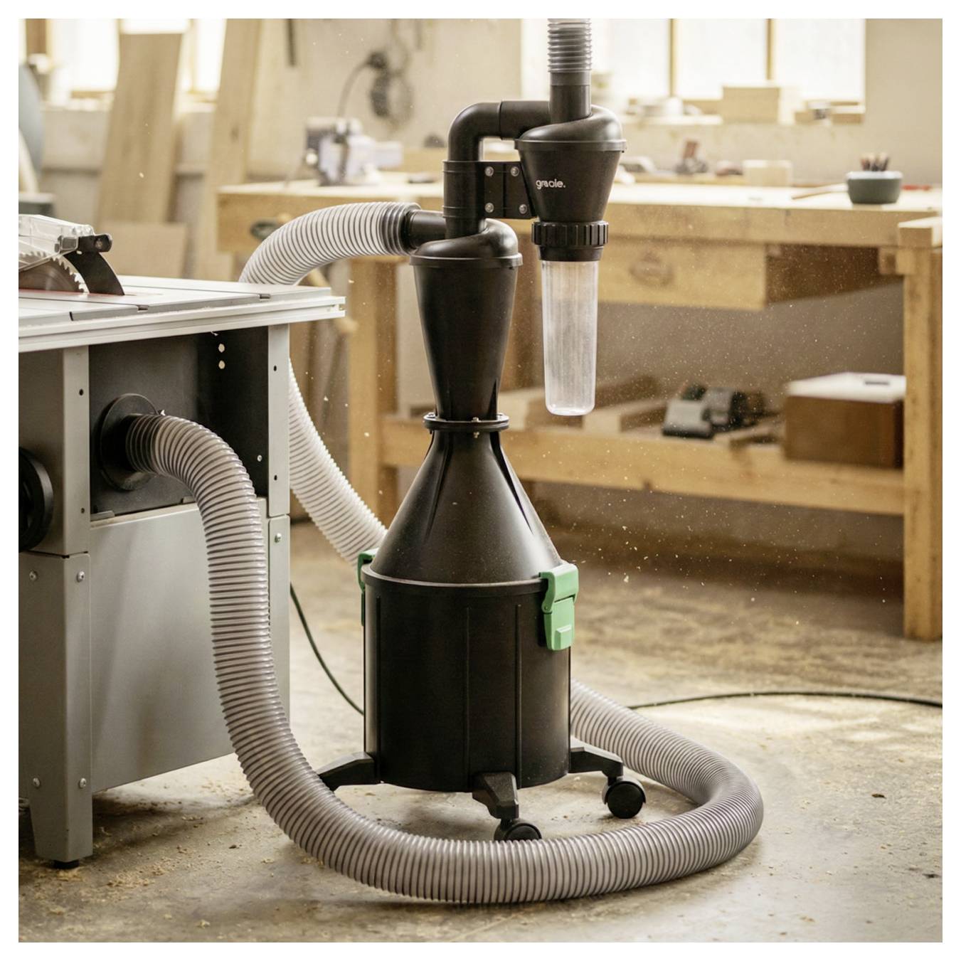 Przenośny odkurzacz pyłu z podłączonymi wężami w warsztacie stoliarskim, używany do usuwania trocin z narzędzi i obszaru roboczego.