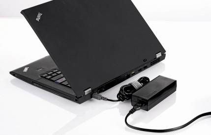 Czarny laptop częściowo otwarty obok adaptera zasilającego na białym tle
