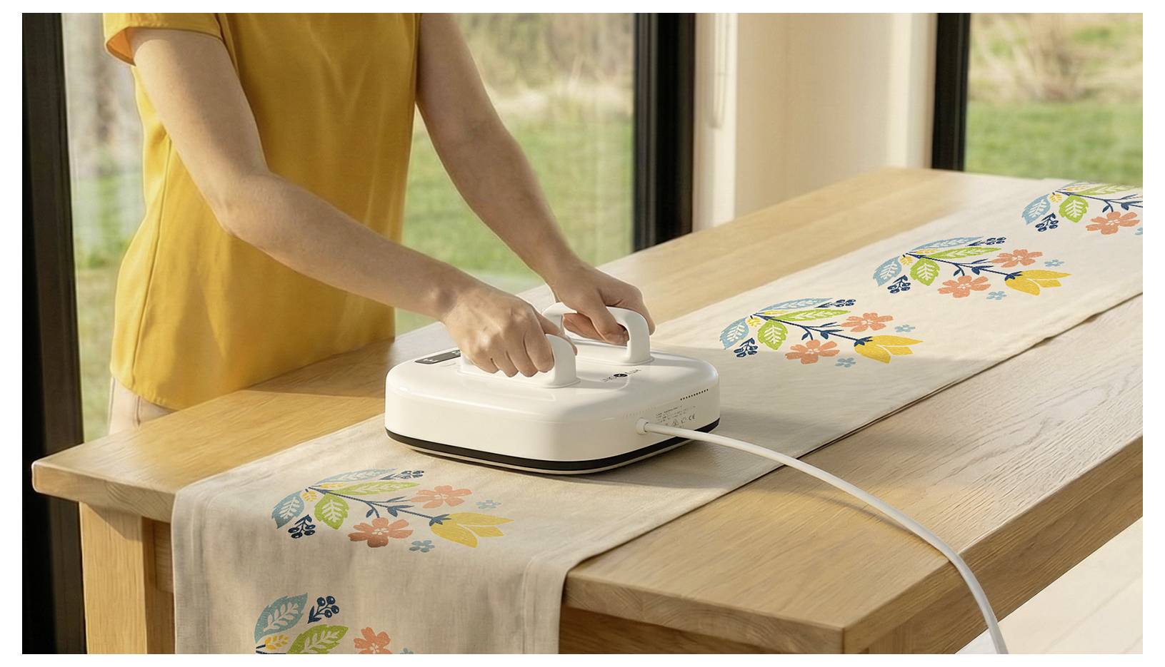 Osoba używająca przenośnej prasownicy termicznej na biegaču stołowego z motywem kwiatowym rozłożonym na drewnianym stole.