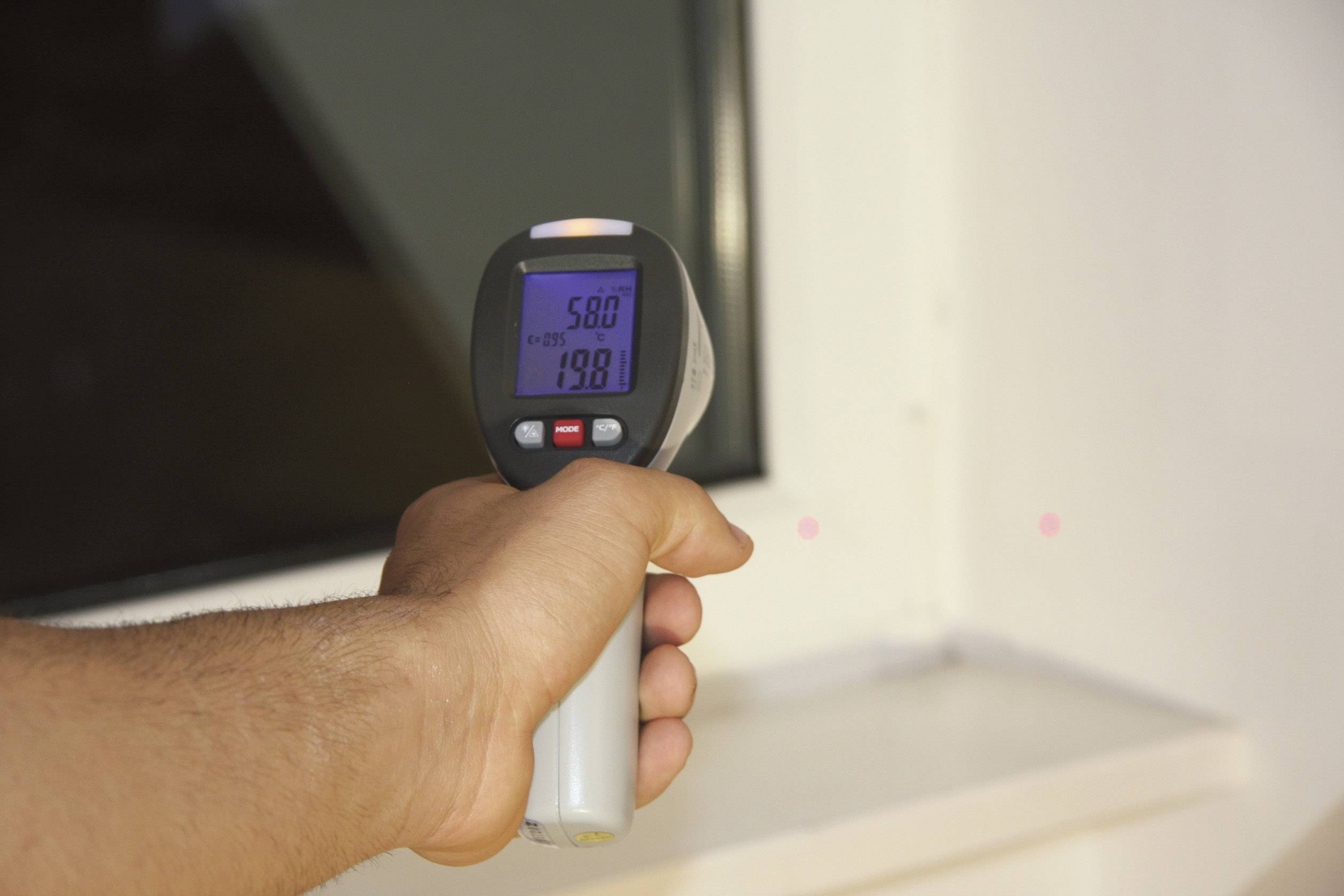 Jedna ręka trzyma termometr na podczerwień skierowany na powierzchnię. Wyświetlacz pokazuje '58,0°C'.