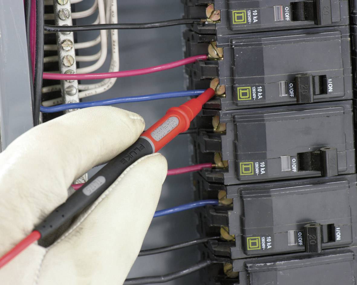 Ręka w rękawicy trzyma próbnik napięcia przy bezpieczniku w elektrycznej rozdzielni bezpieczników, dokonując sprawdzenia napięcia.