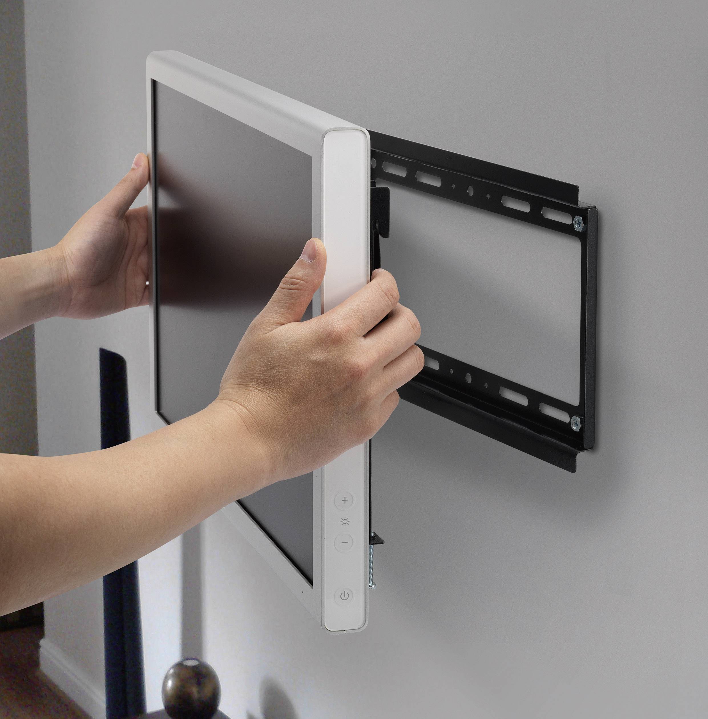 Osoba mocuje telewizor płaski na uchwycie ściennym. Ekran jest trzymany obiema rękami, podczas gdy wsuwa się go w mocowanie.