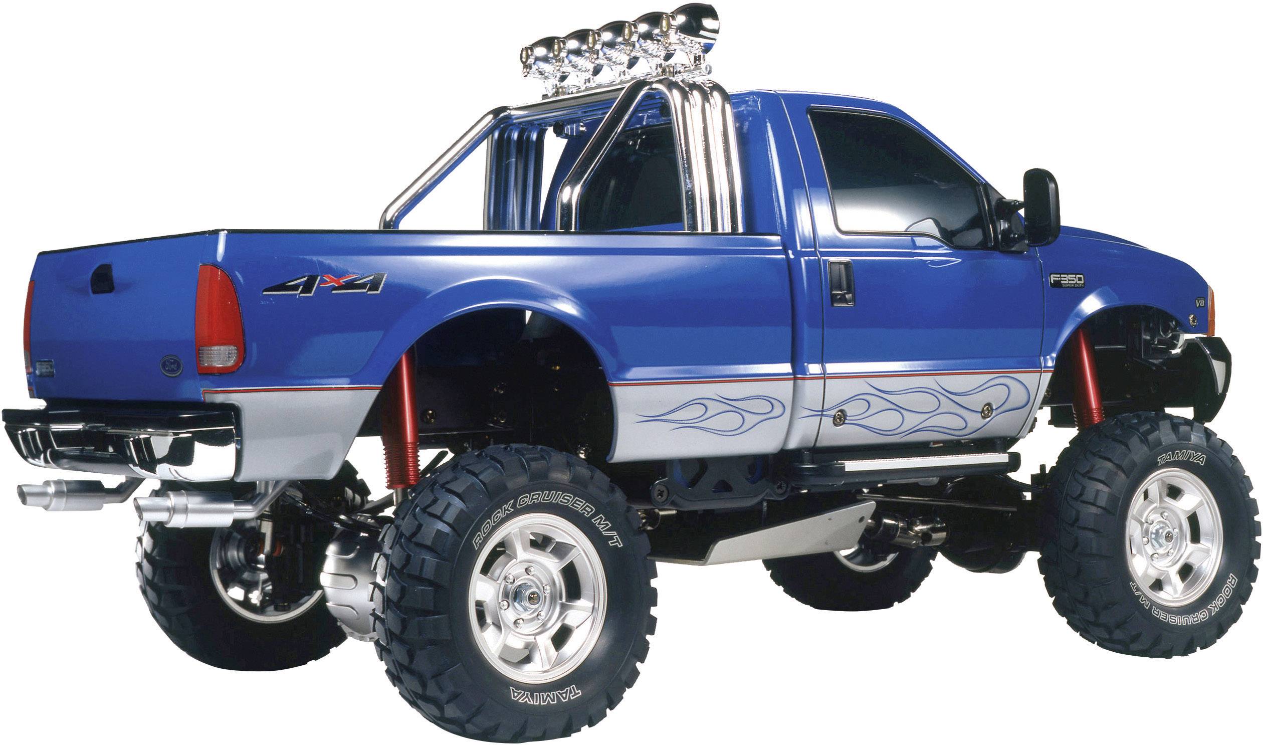 Niebieski, podniesiony pickup z dużymi oponami i płomiennymi wzorami na burtach, zaparkowany na białej powierzchni.