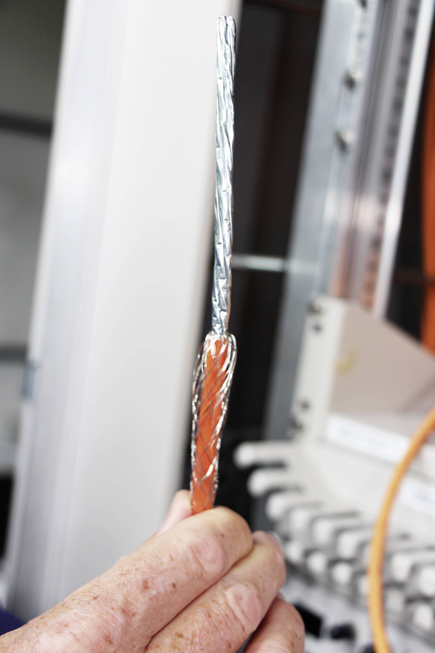 Dłoń trzyma kabel z pomarańczową izolacją i widocznym srebrnym oplotem, prawdopodobnie podczas instalacji.