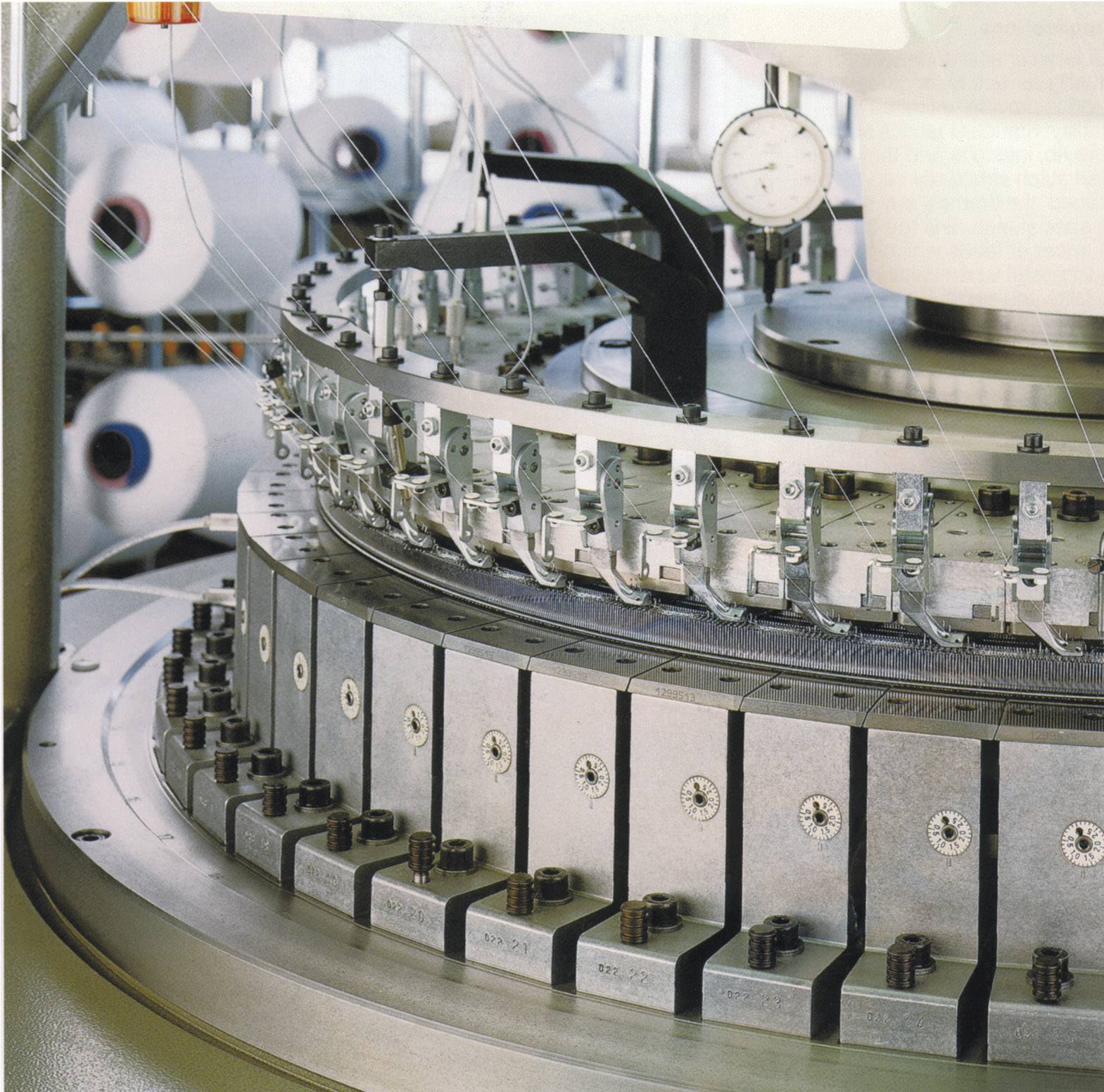 Maszyna przemysłowa w fabryce włókienniczej. Widoczna jest przednia strona z okrągłą obudową pełną szpul i wyposażenia technicznego.