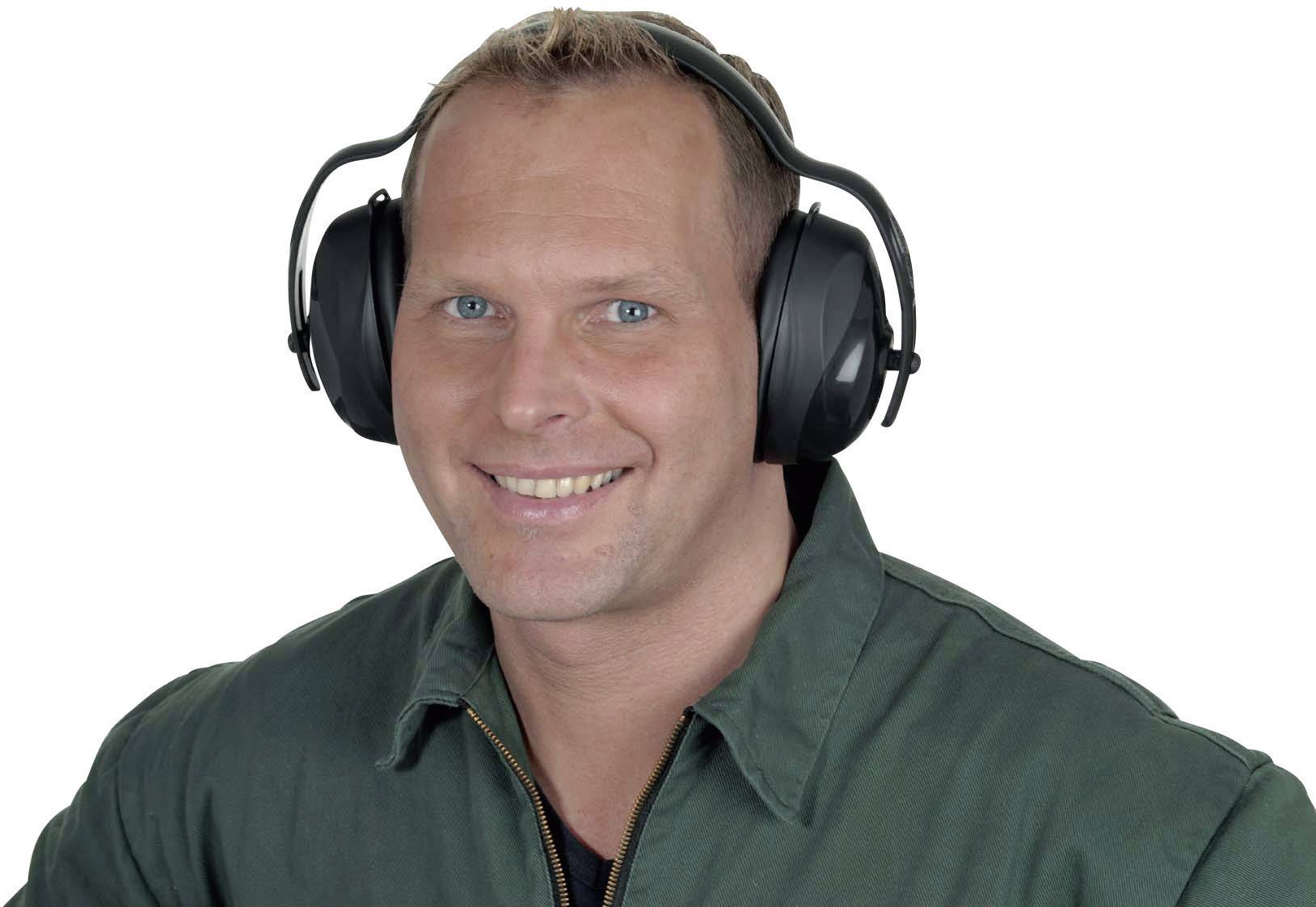 Osoba nosi nauszniki ochronne i uśmiecha się, ubrana w zieloną kurtkę roboczą.