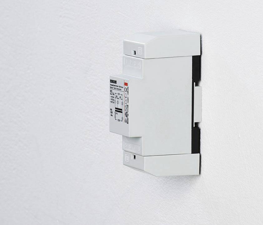 Biały, prostokątny włącznik światła jest zamontowany na białej ścianie. Na przełączniku widnieją szczegóły techniczne na etykiecie.