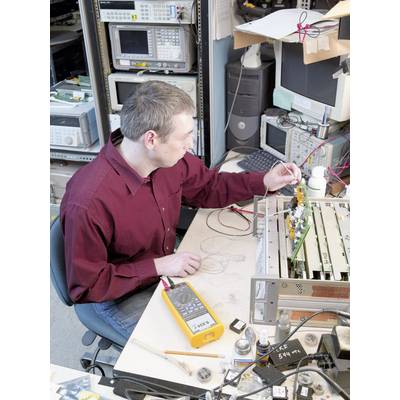 Osoba w laboratorium technicznym pracuje nad płytką drukowaną, mając wokół elektroniczne przyrządy pomiarowe i narzędzia rozłożone na stole.