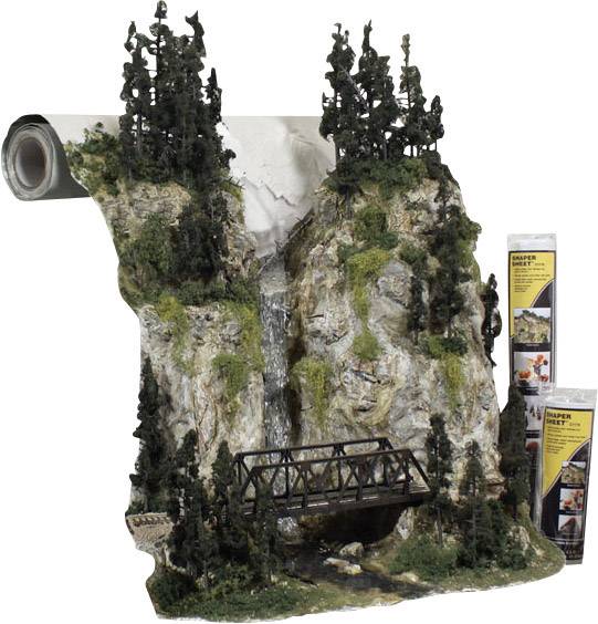 Model terenu przedstawia skalistą krajobraz z wysokimi sosnami, wodospadem i mostem. Akcesoria do kolejki modelarskiej w skali.