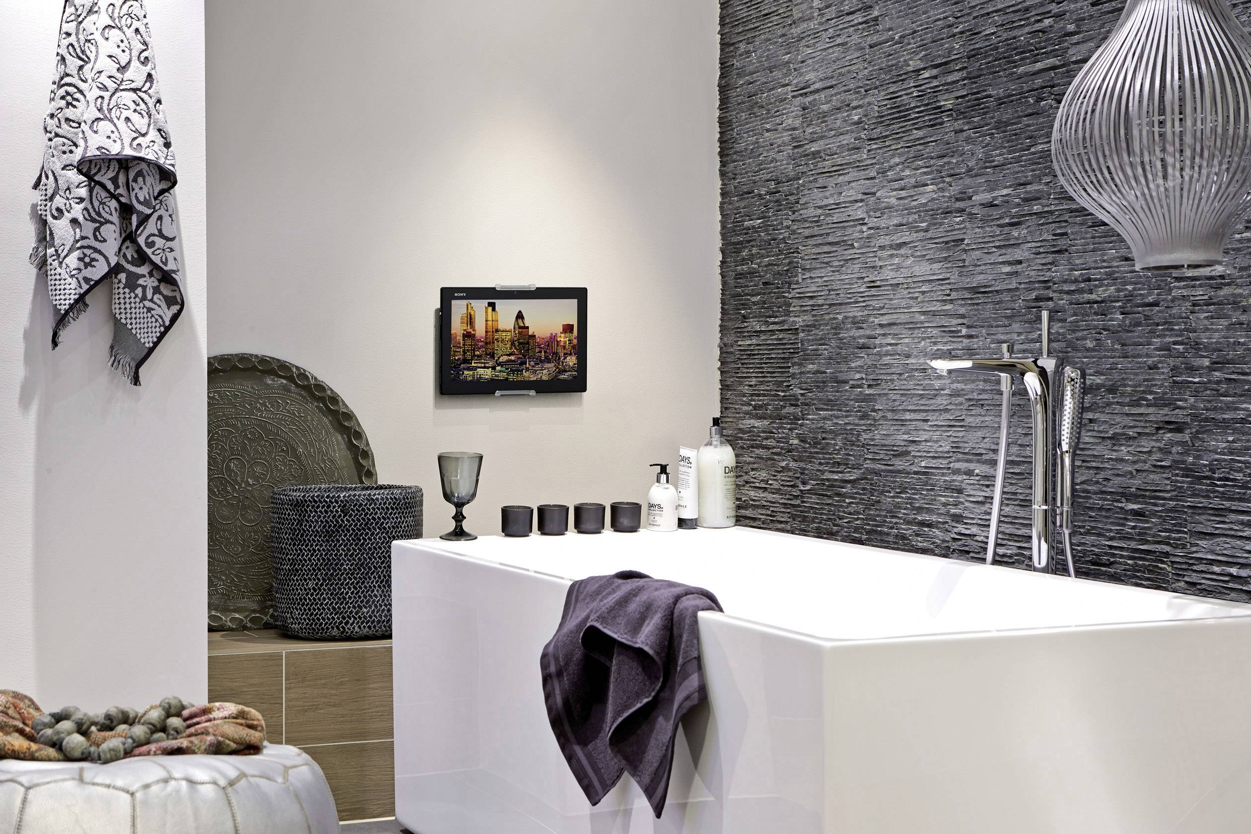 Nowoczesna łazienka z wolnostojącą wanną, czarną okładziną ścienną, dekoracyjnymi ręcznikami i stylowym oświetleniem.