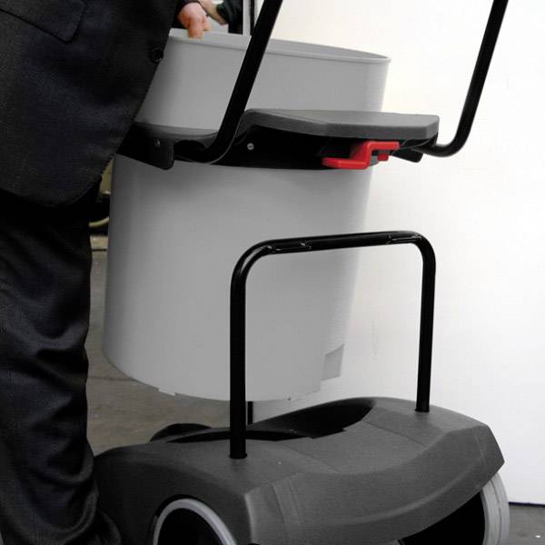 Osoba w formalnym garniturze podnosi szary wiadro na czarnym wózku do sprzątania.