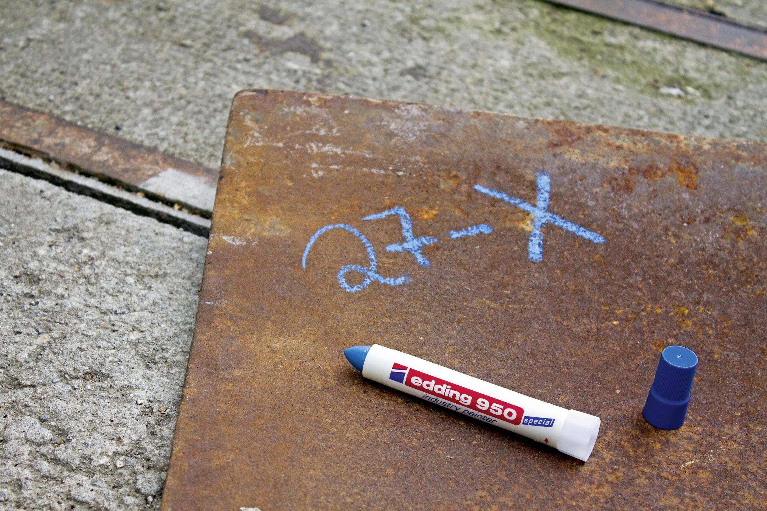 Kawałek metalu na betonowej podłodze, opisany niebieską kredą: '27-X'. Obok leży otwarty niebieski marker.