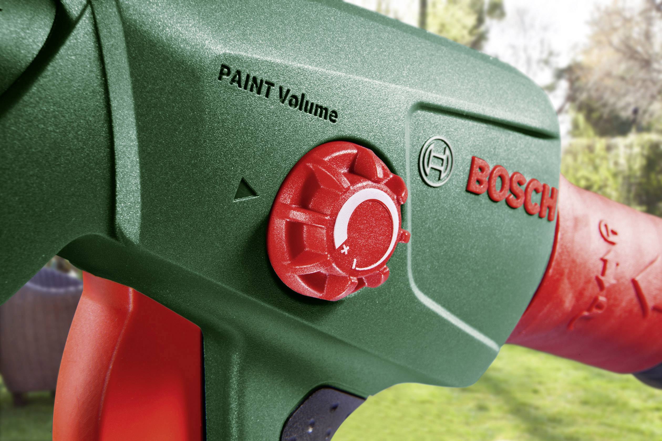 Zbliżenie zielonego pistoletu natryskowego marki Bosch z czerwonym pokrętłem 'PAINT Volume' do regulacji ilości farby.