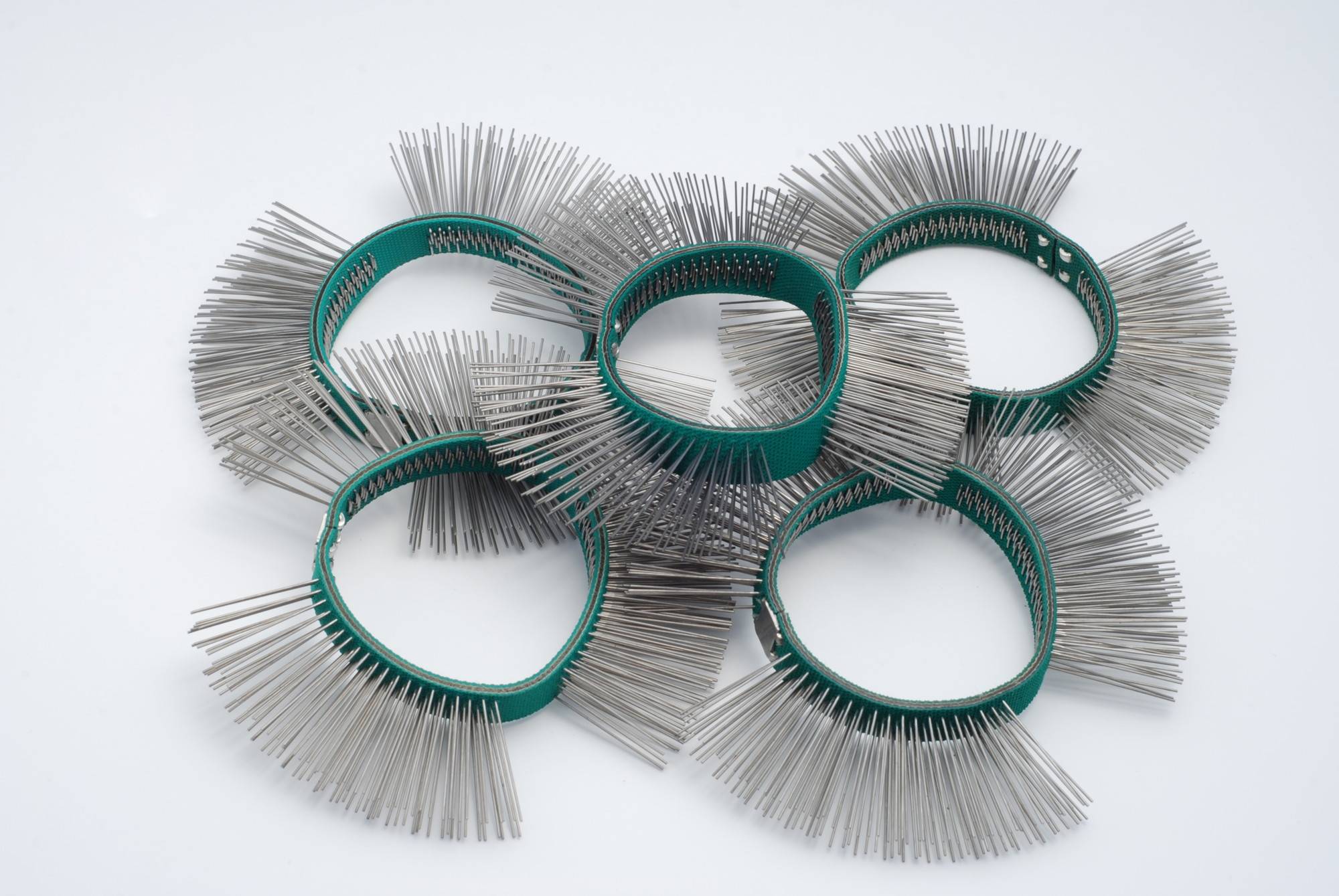 Sześć zielonych, okrągłych igłowych szczotek leży jedna na drugiej na białym tle. Mają gęste rzędy włosia wokół każdego pierścienia.