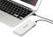 Laptop jest podłączony za pomocą kabla USB do białego powerbanku, który leży na płaskiej powierzchni.