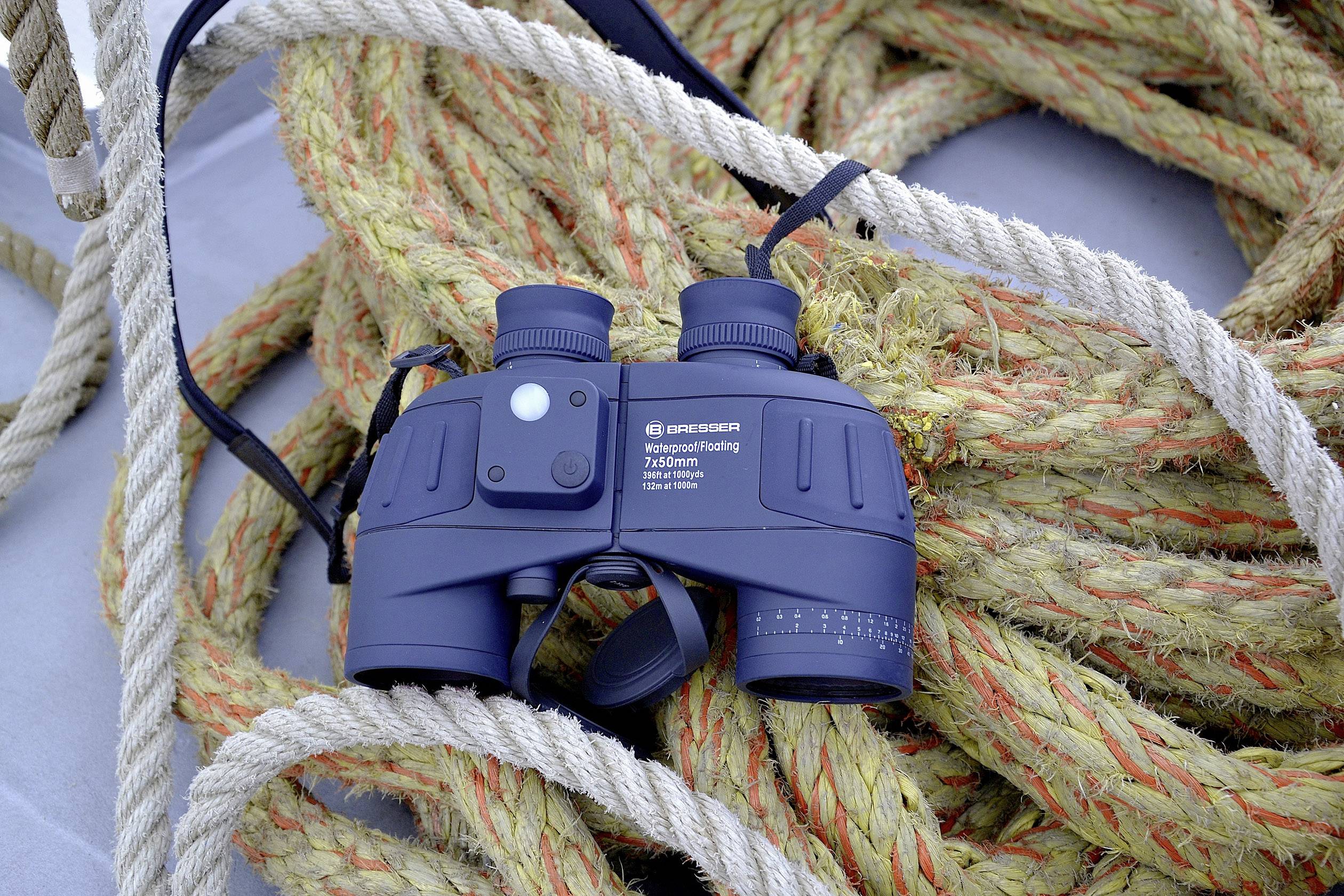 Lornetka leży na stosie lin. Jest to lornetka w kolorze granatowym z napisem, otoczona grubymi linami.