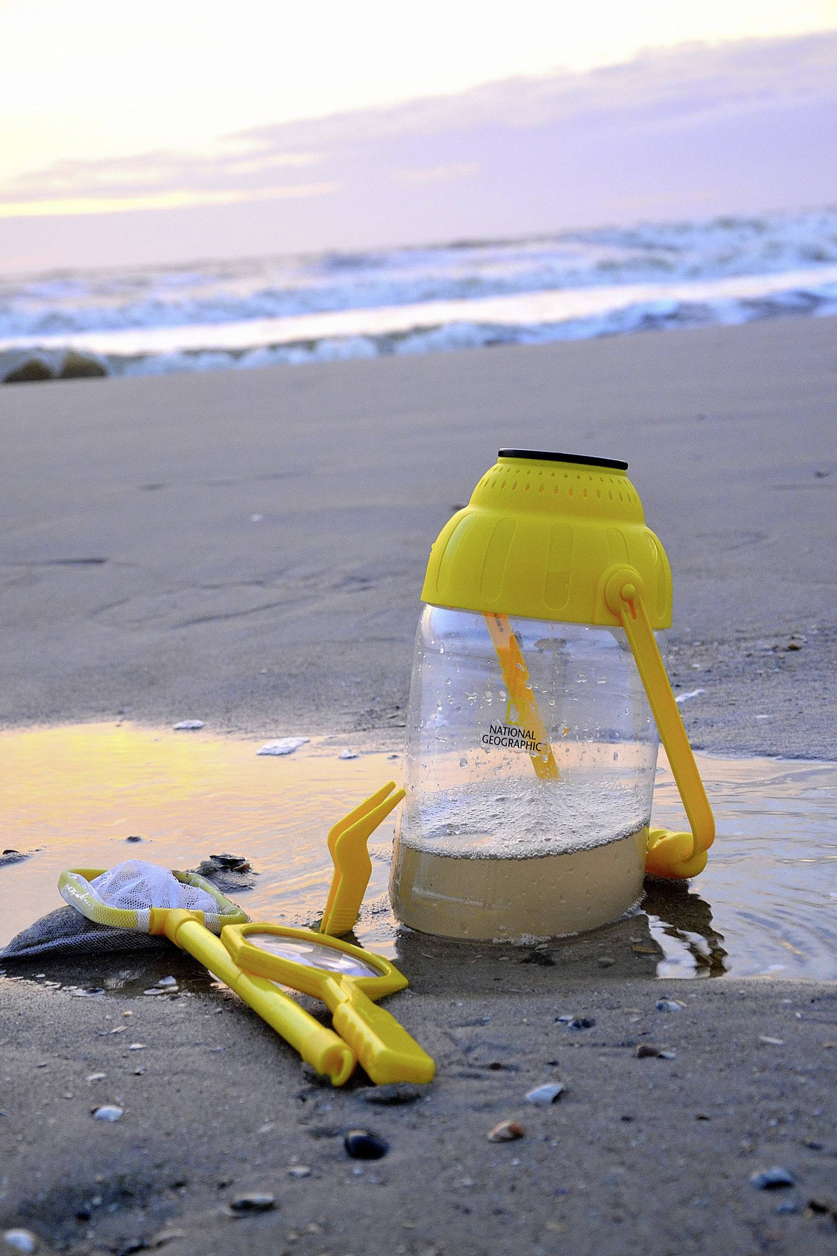 Żółty plastikowy pojemnik na zabawki plażowe i łopatki leżą na plaży o zachodzie słońca, z falami w tle.