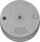 Biały czujnik dymu o okrągłym kształcie, z widocznym głośnikiem i przyciskiem testowym. Chroni przed zadymieniem i pożarami.