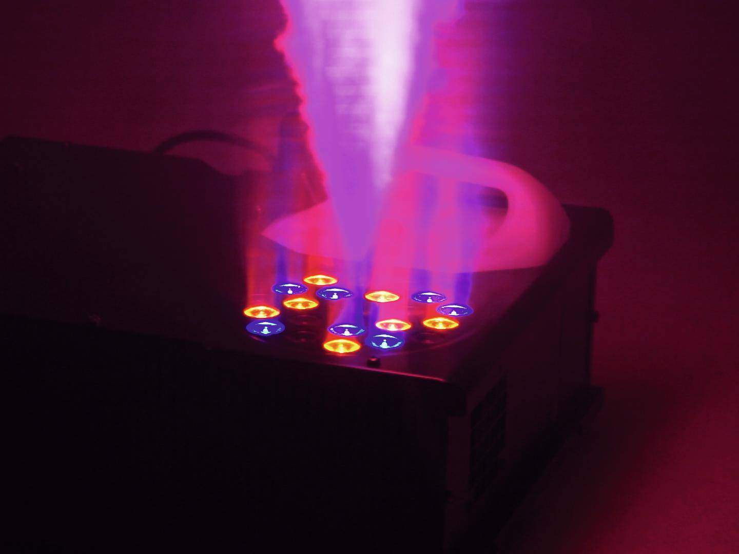 Maszyna mgielna emituje czerwone i niebieskie światło w ciemności, wyrzucając dynamiczny słup mgły w powietrze.