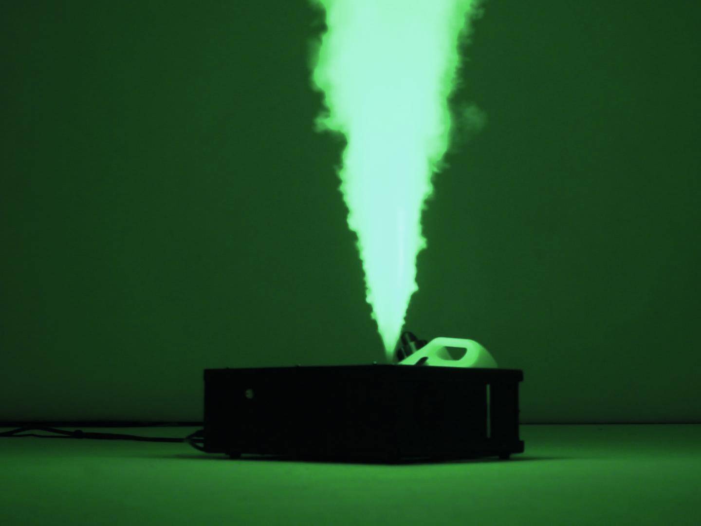 Czarne urządzenie wyrzuca grubą zieloną chmurę dymu pionowo w górę w zaciemnionym pomieszczeniu.