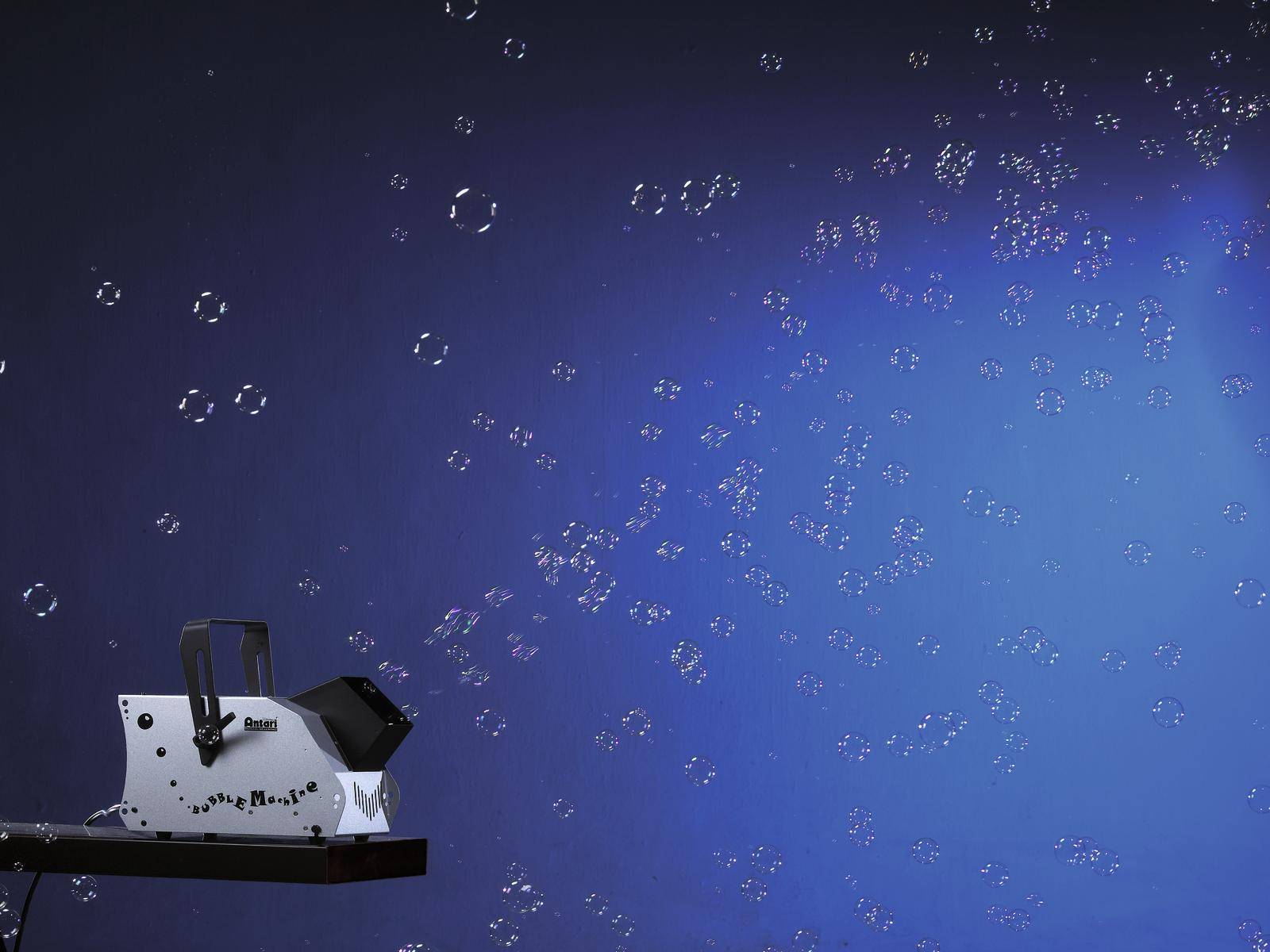 Maszyna do robienia baniek mydlanych wytwarza wiele małych baniek, które unoszą się w powietrzu na niebieskim tle.