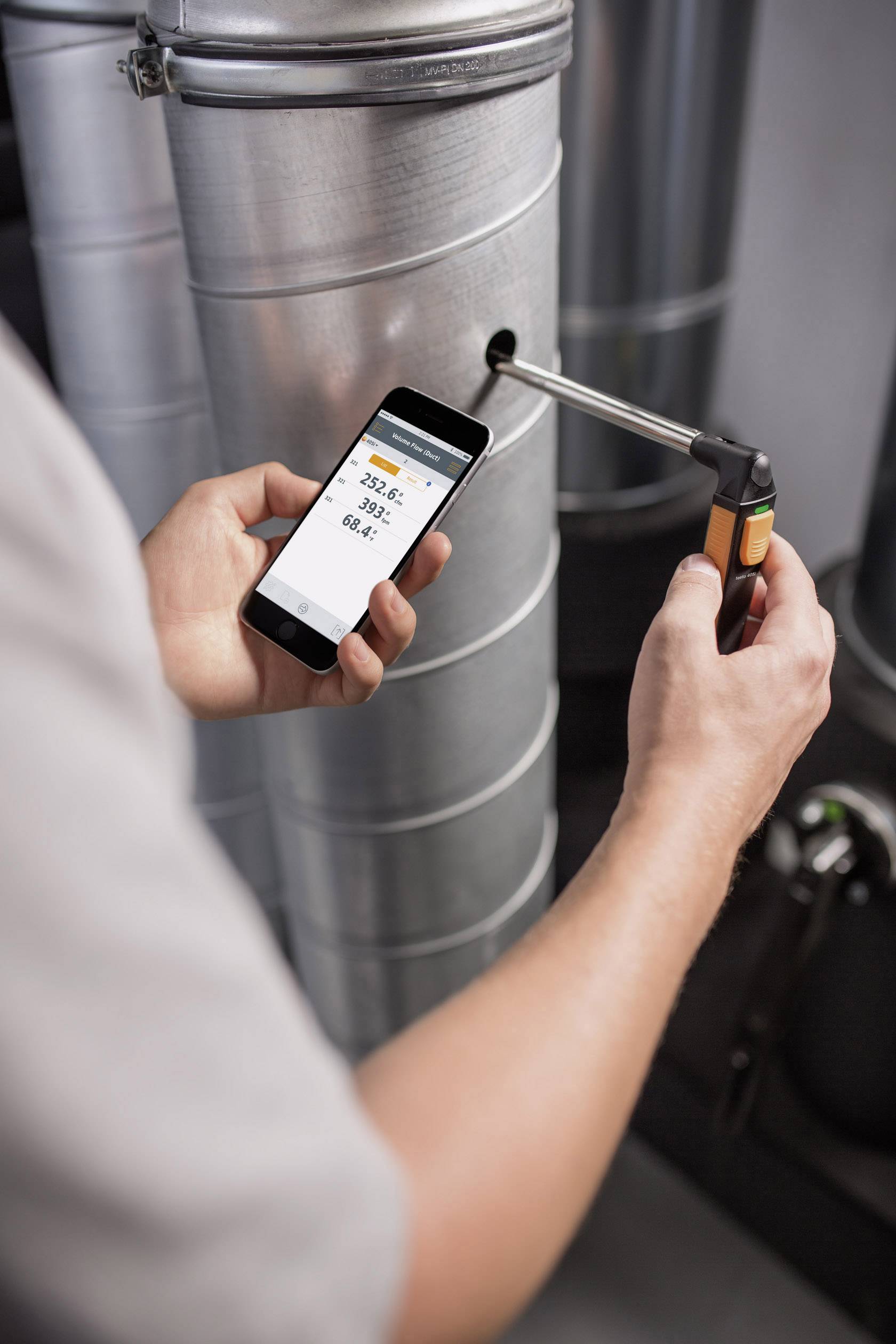 Osoba mierzy temperaturę rury za pomocą urządzenia. Smartfon wyświetla temperaturę odczytaną jako 23,5 °C.