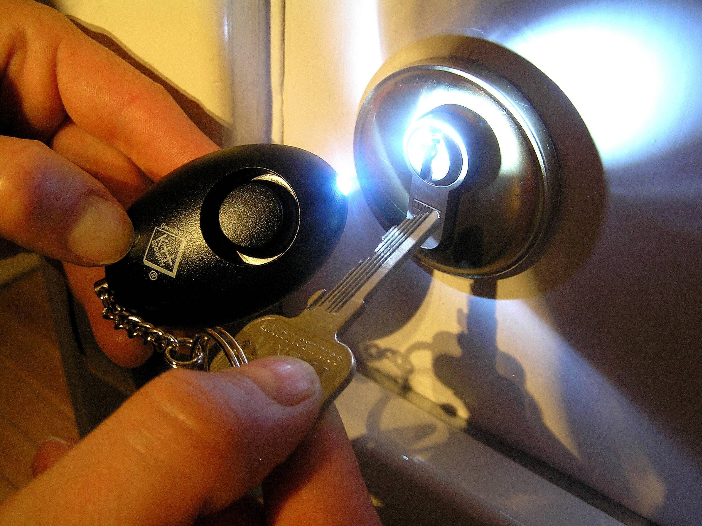 Ręka trzyma klucz z latarką, próbując otworzyć zamek w ciemności.