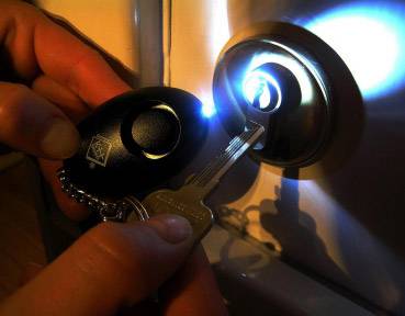 Dłoń trzyma świecący brelok i klucz, który jest wkładany do zamka w drzwiach.